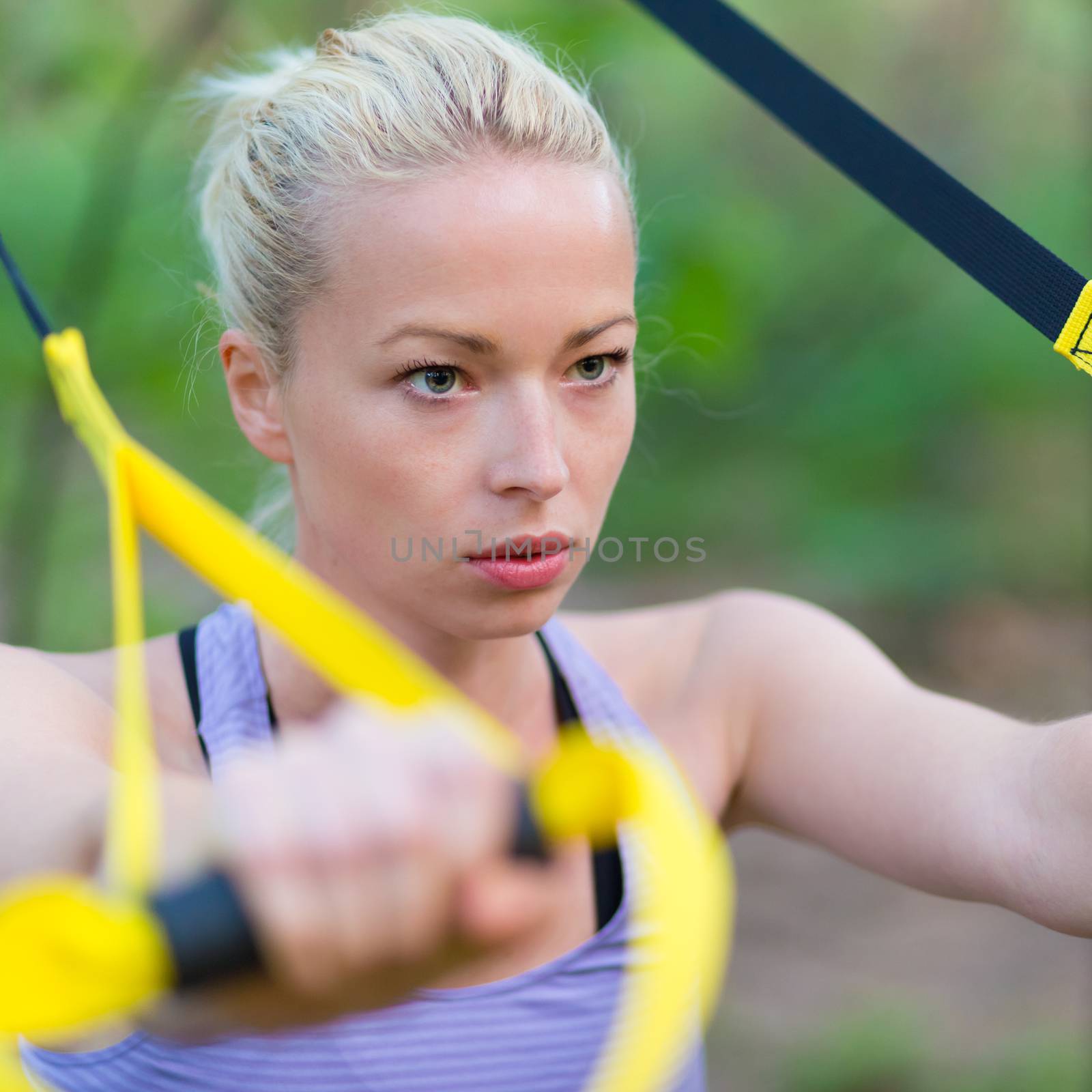 Young attractive woman does suspension training with fitness straps outdoors in the nature.