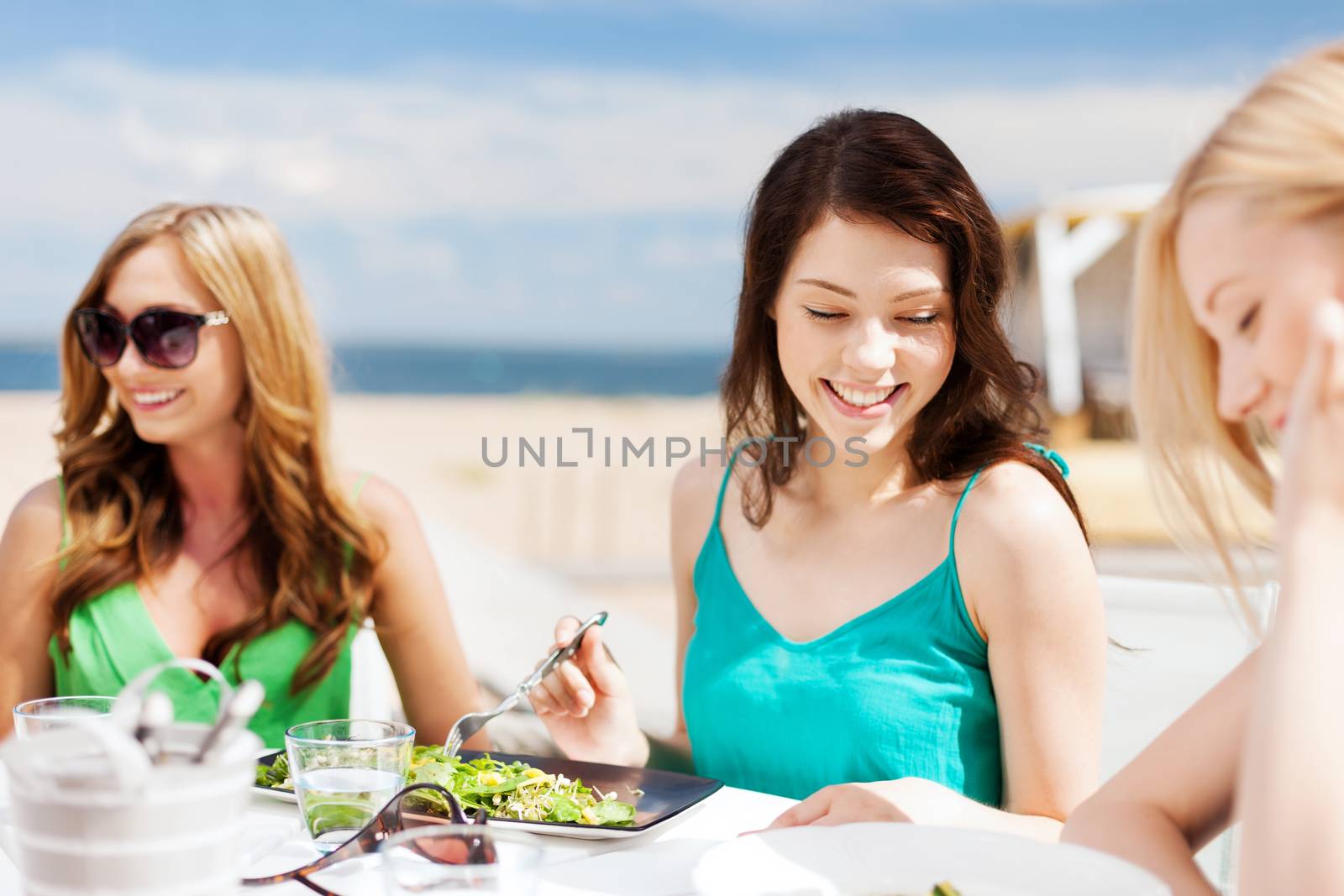 summer holidays and vacation - girls eating and drinking in cafe on the beach