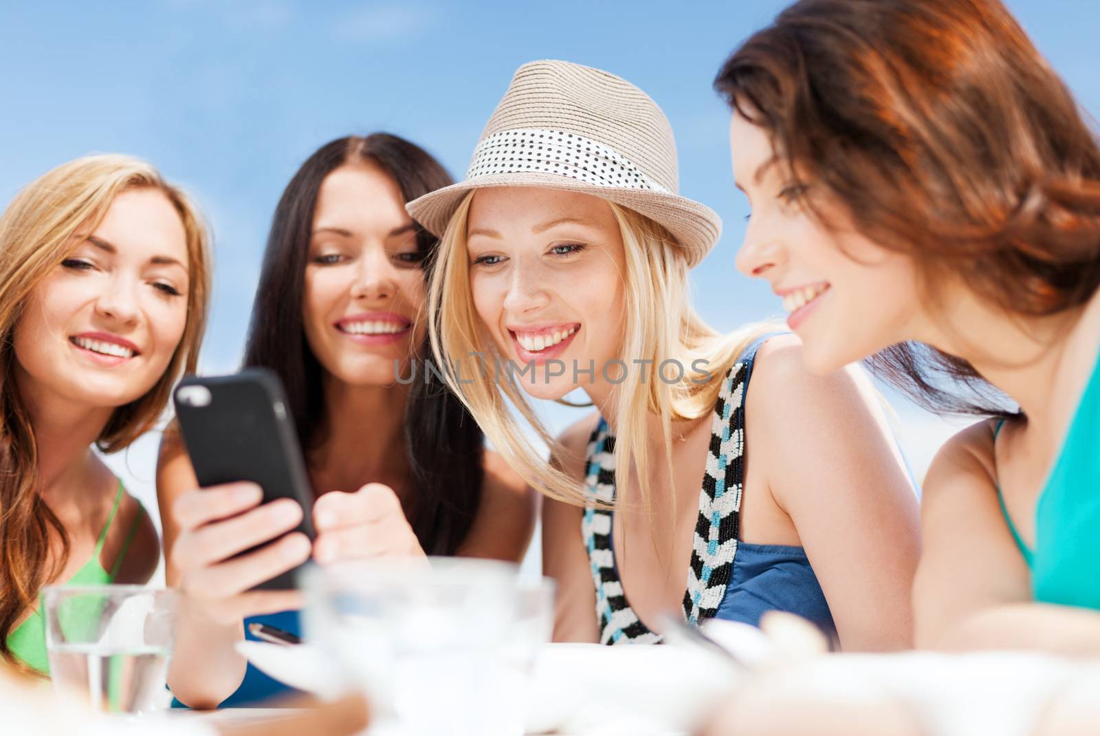 summer holidays, vacation and technology - girls looking at smartphone in cafe on the beach