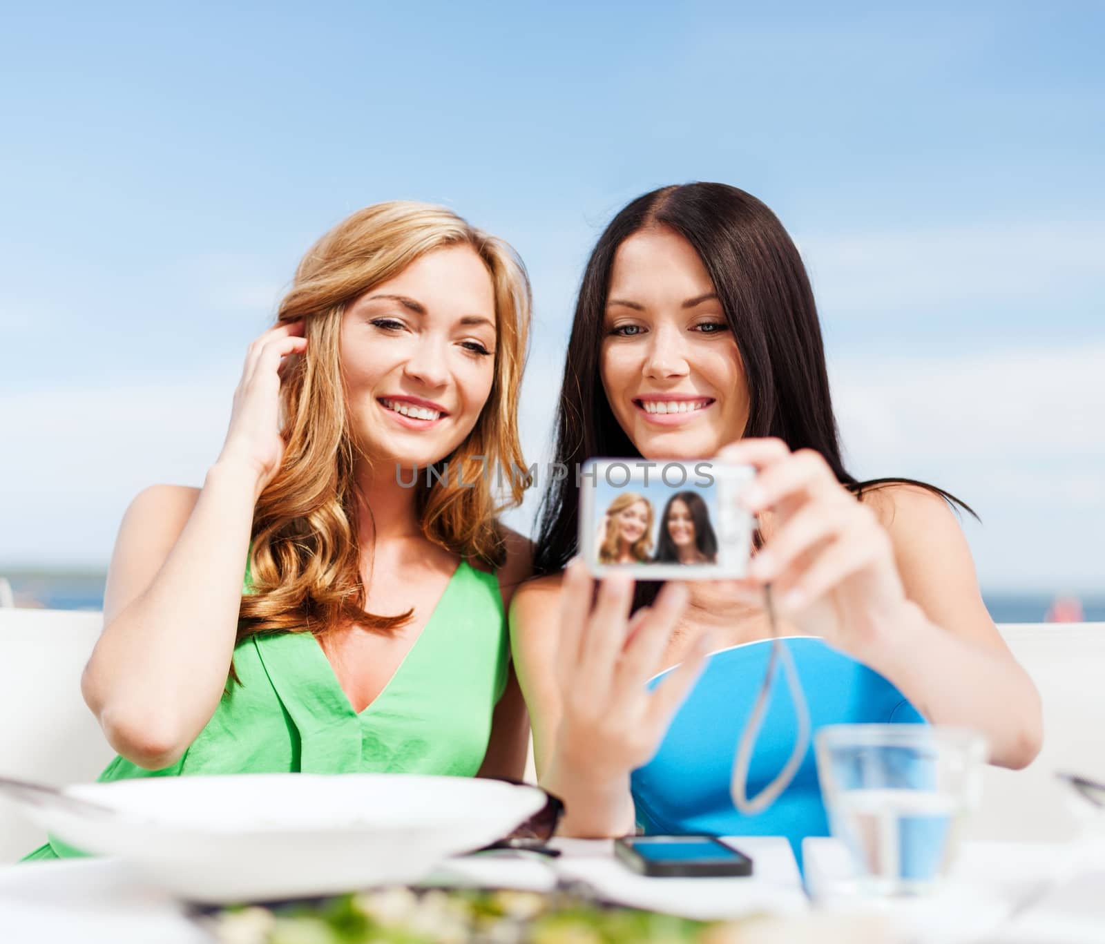 summer holidays, vacation and technology - girls taking photo with digital camera in cafe on the beach