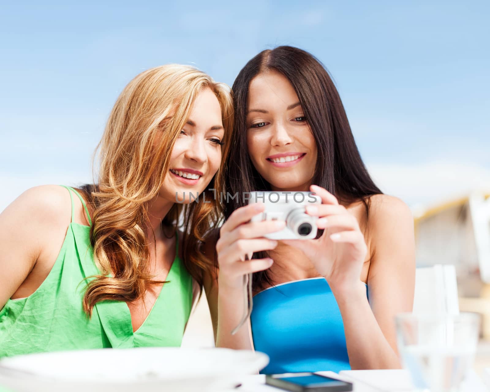 summer holidays, vacation and technology - girls looking at digital camera in cafe on the beach