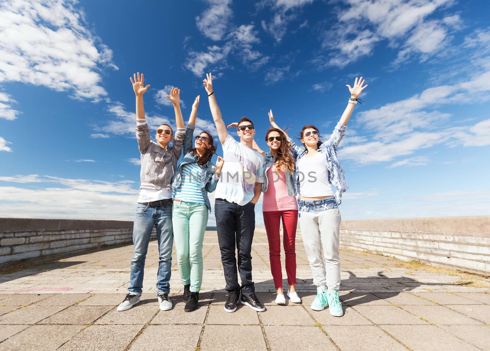 summer holidays and teenage concept - group of teenagers holding hands up outside