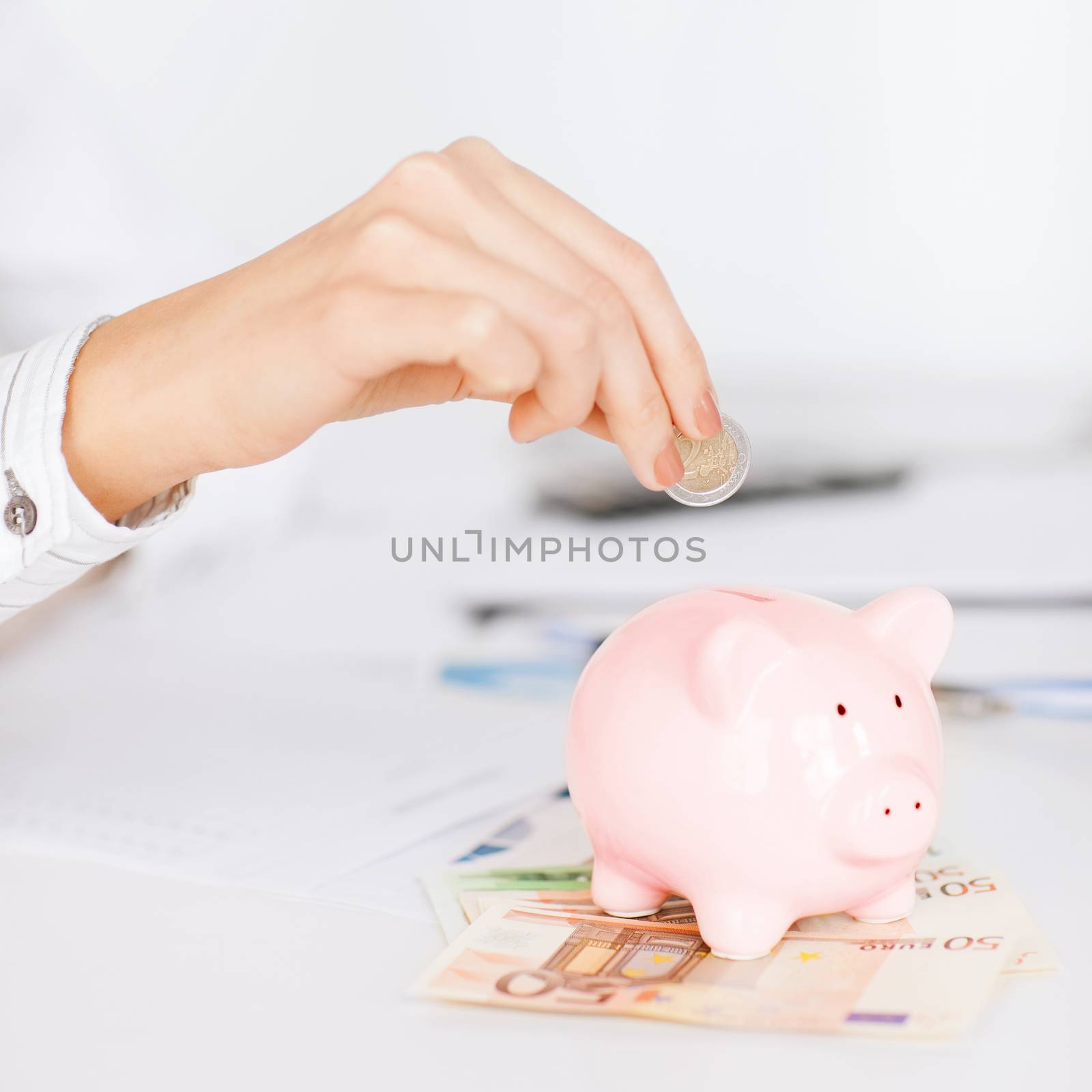 woman hand putting coin into small piggy bank by dolgachov