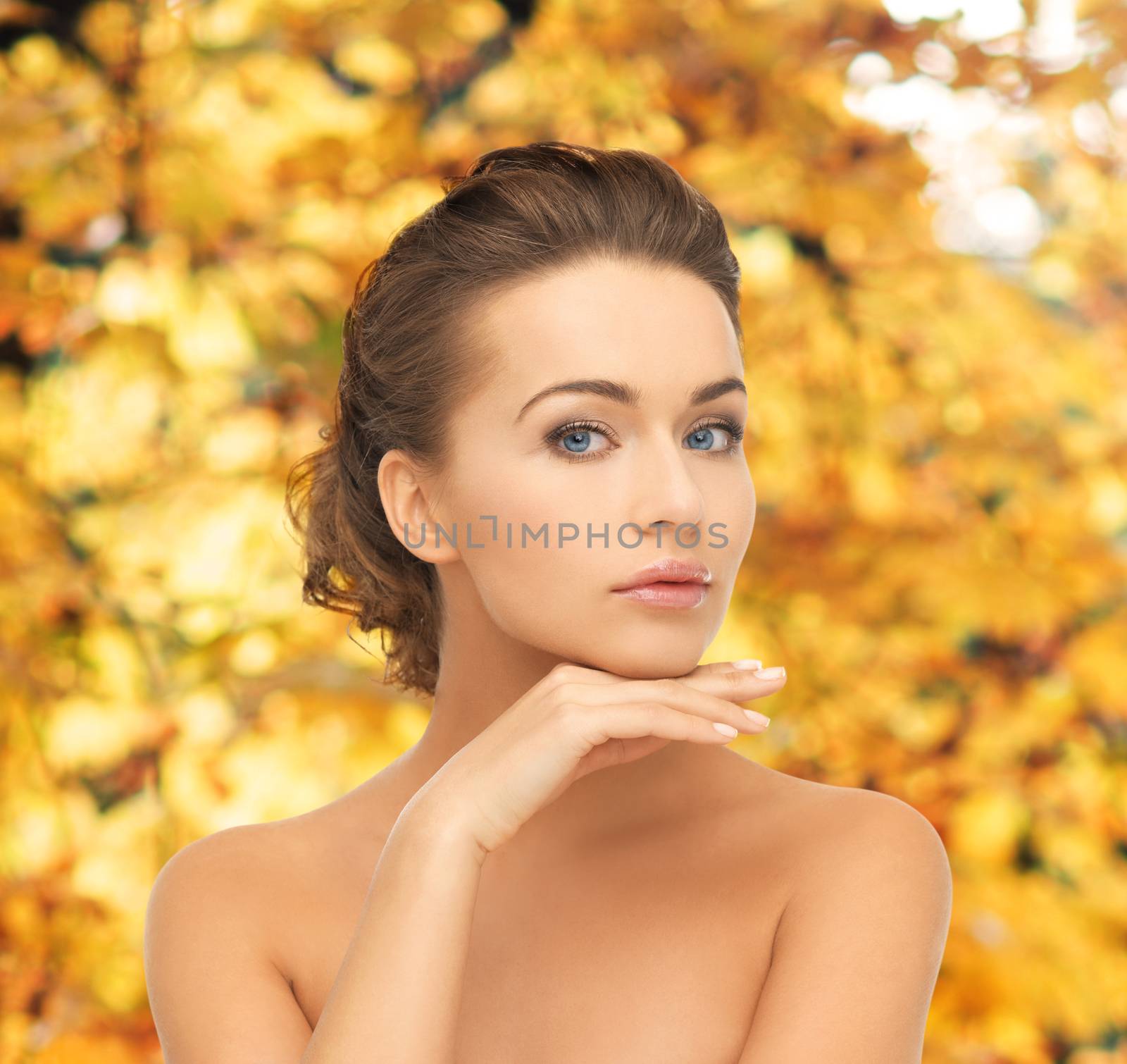 health and beauty concept - face and hands of beautiful woman with updo over yellow autumn leaves background