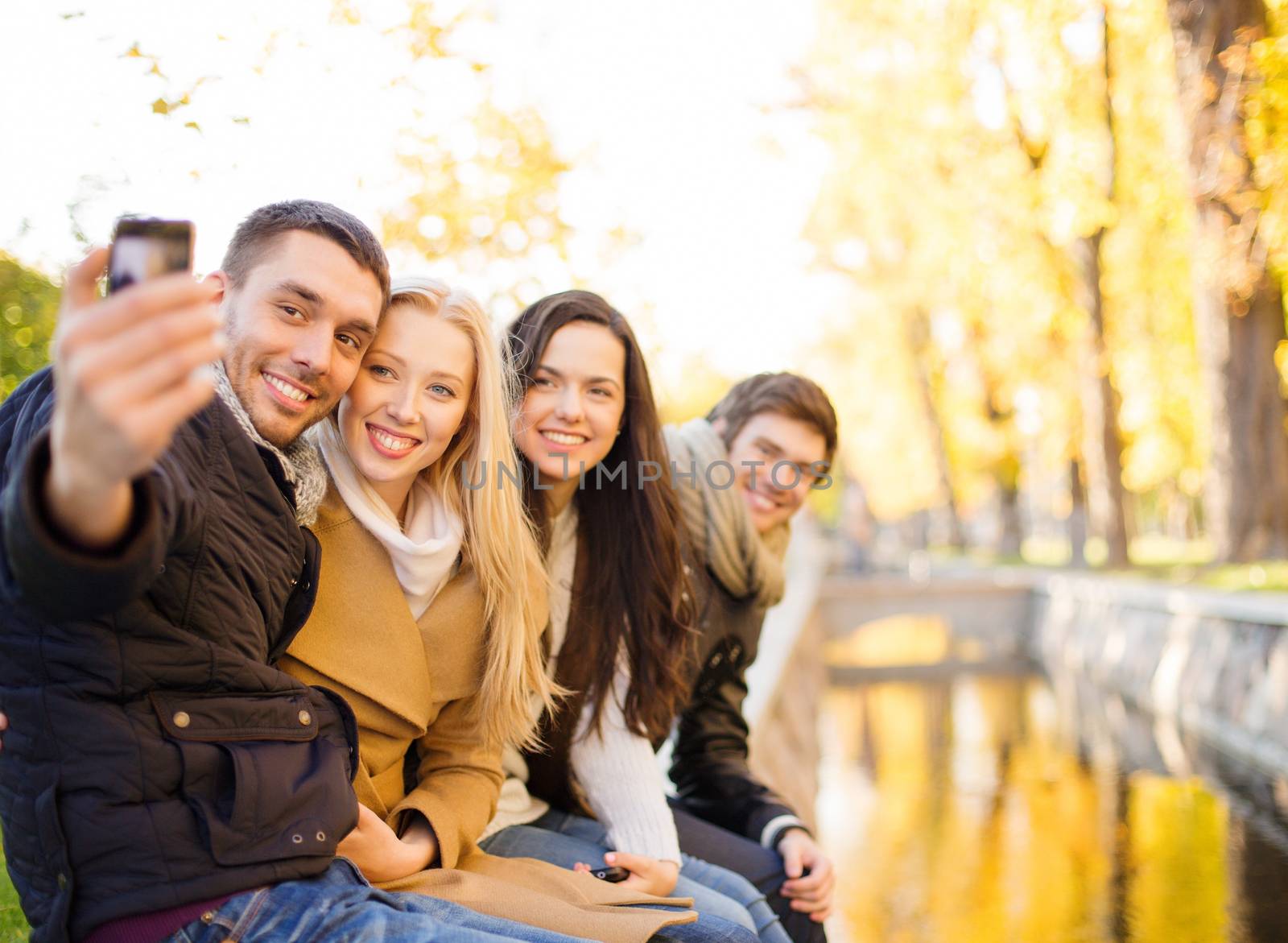 summer, holidays, vacation, travel and tourism concept - group of friends or couples having fun with smartphone photo camera in autumn park