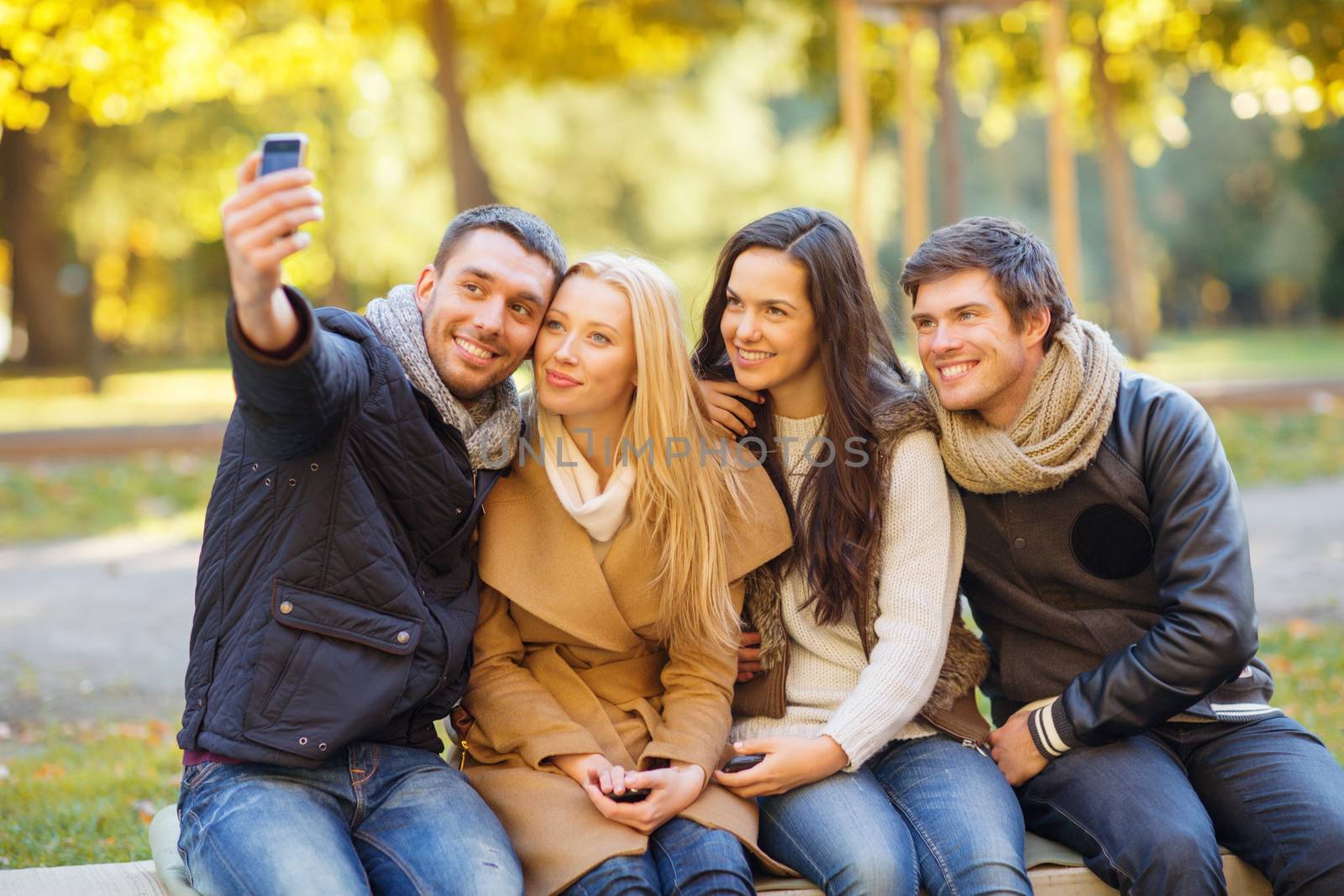 summer, holidays, vacation, travel and tourism concept - group of friends or couples having fun with smartphone photo camera in autumn park