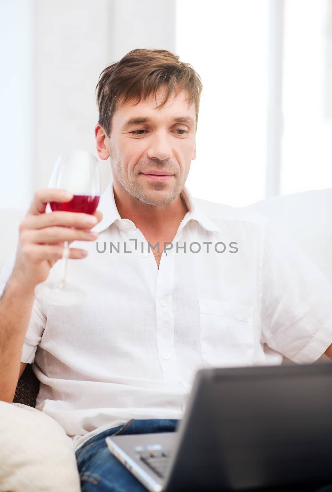 man with laptop computer and glass of rose wine by dolgachov