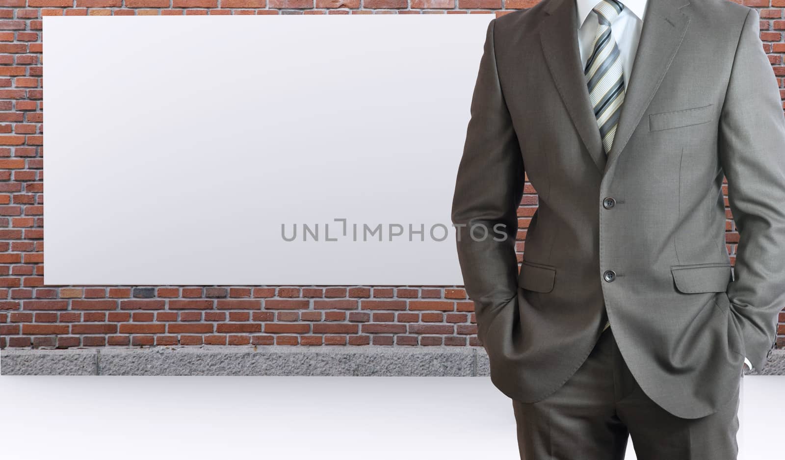 Businessman standing with hands in pockets. Brick wall and white placard as backdrop