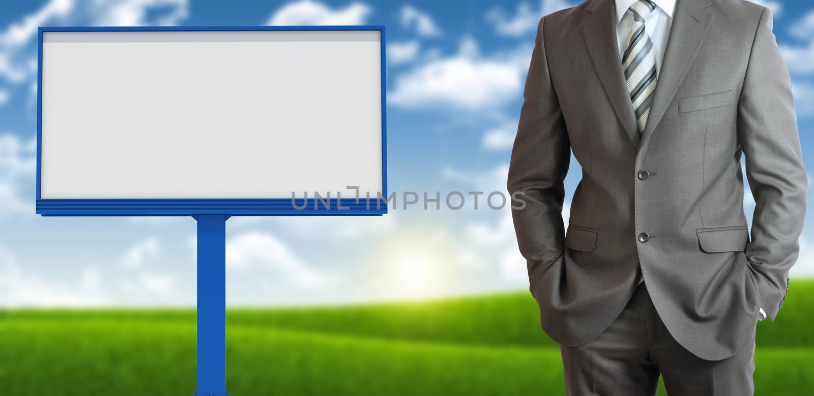 Businessman standing with hands in pockets. Blank billboard, blue sky and green grass as backdrop