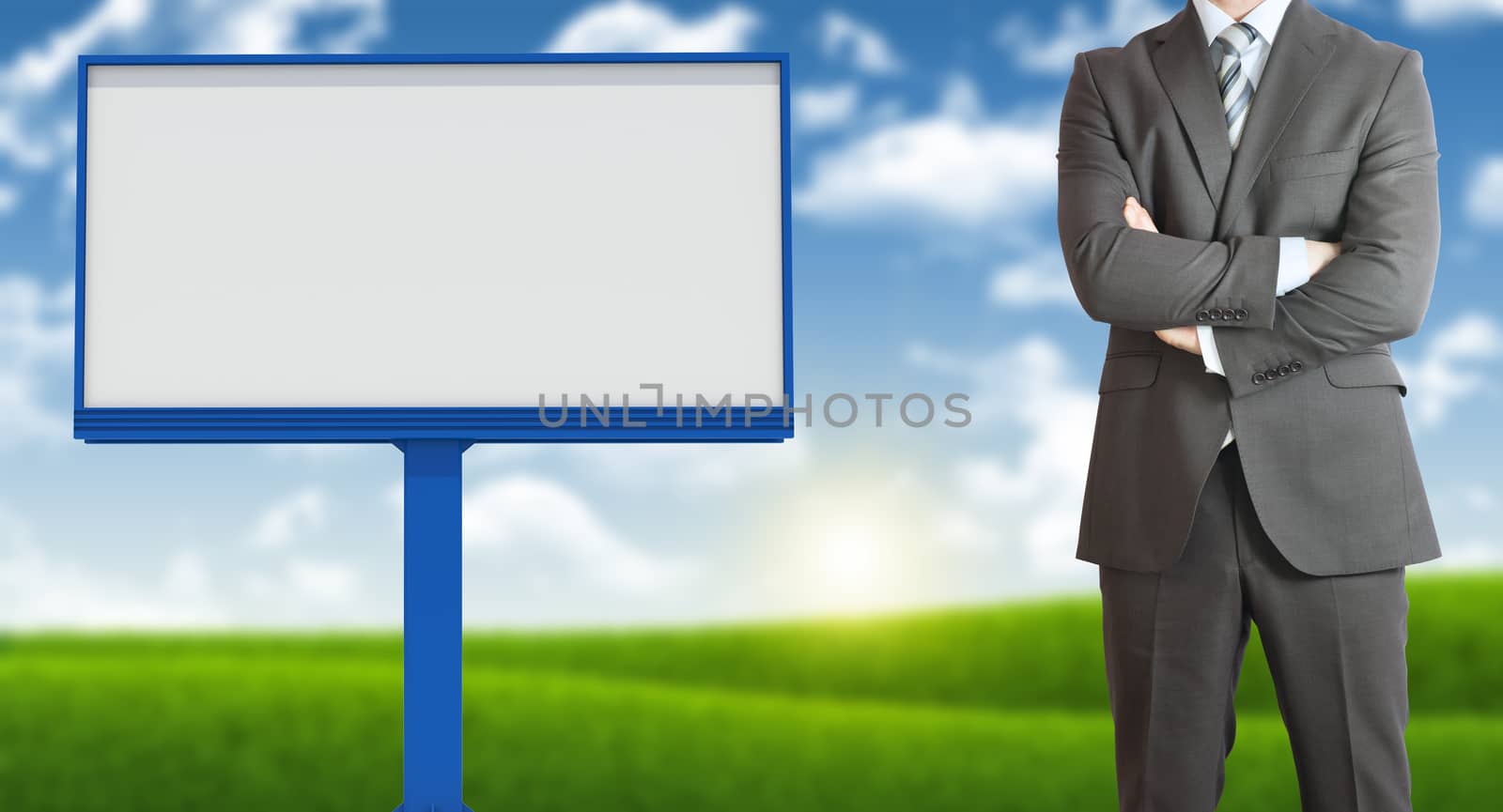 Businessman standing with his arms crossed. Blank billboard, blue sky and green grass as backdrop