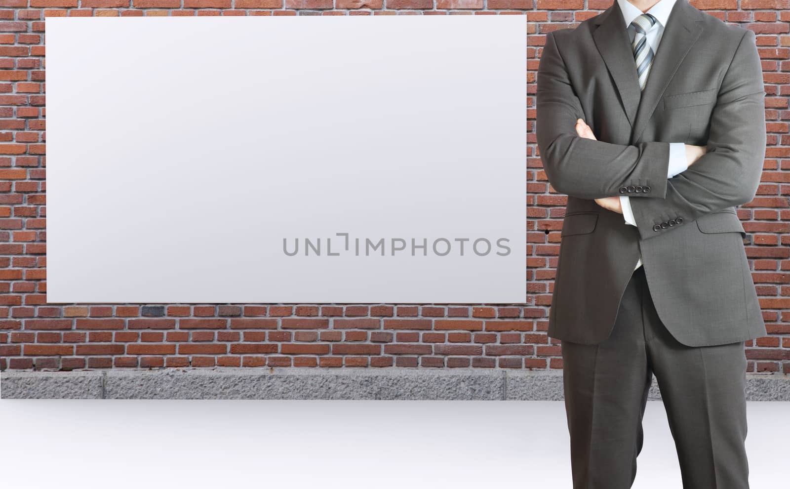 Businessman standing with his arms crossed. Brick wall and white placard as backdrop