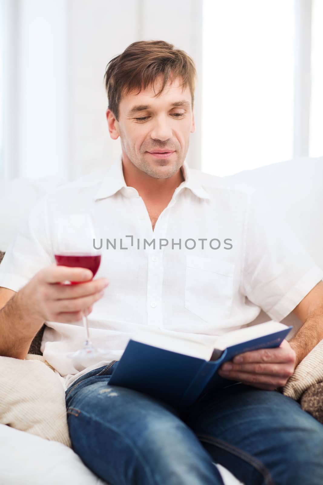 leisure, drinks, retirement, education and lifestyle concept - happy man with book and glass of rose wine at home