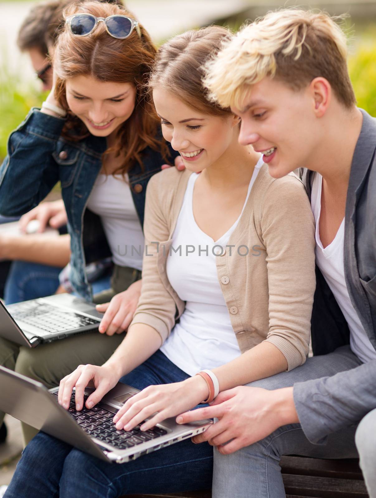 summer, internet, education, campus and teenage concept - group of students or teenagers with laptop computers hanging out