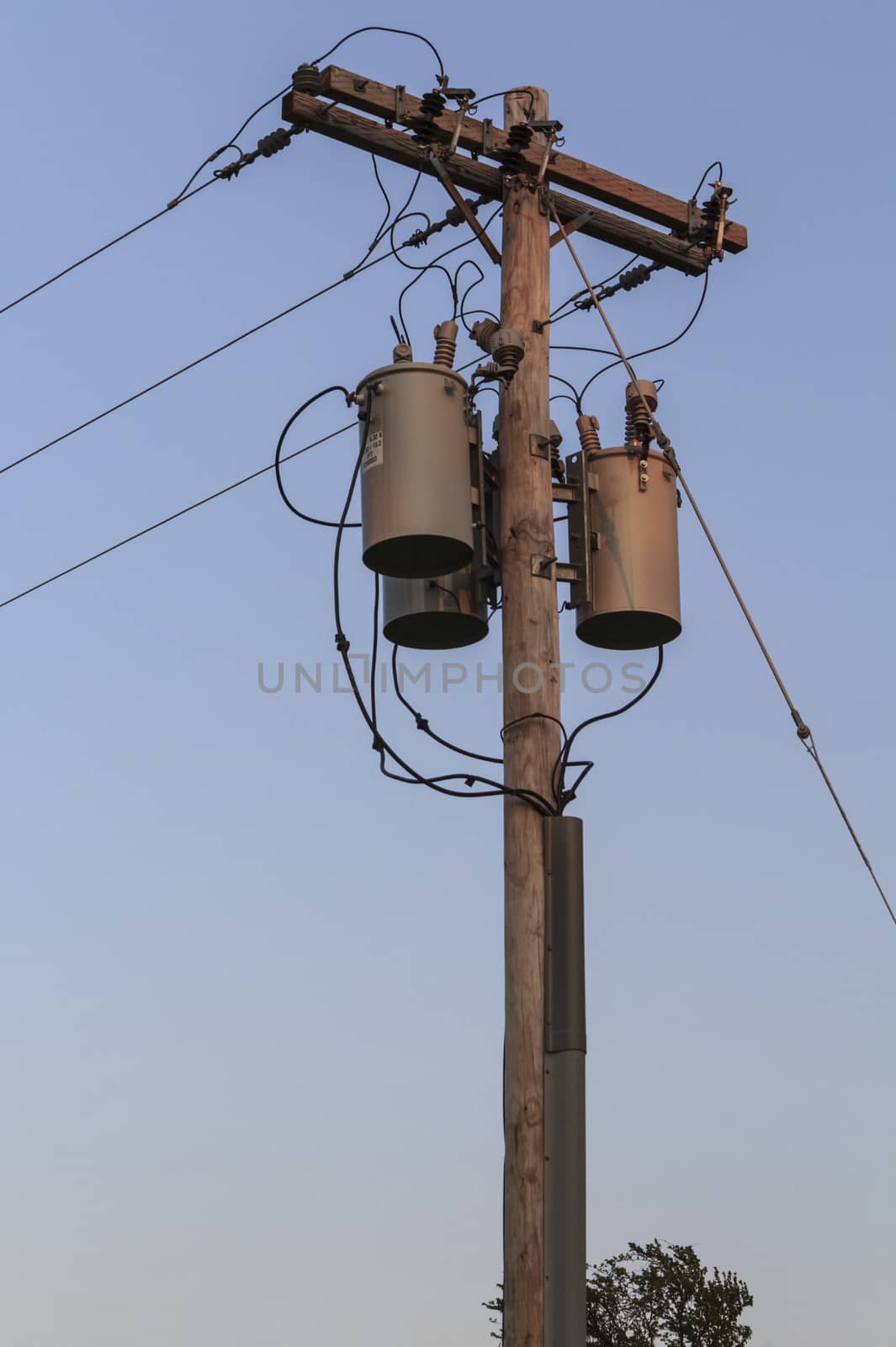 Wooden electric pole with many wire cables and grey metal transformers. 