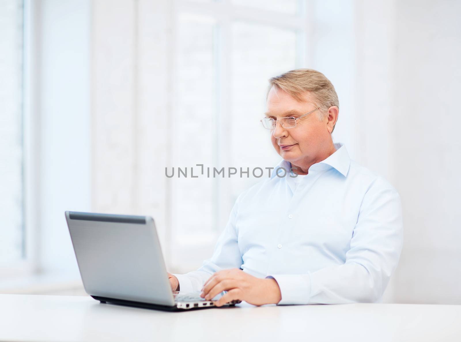 technology, oldness and lifestyle concept - old man in eyeglasses working with laptop computer at home
