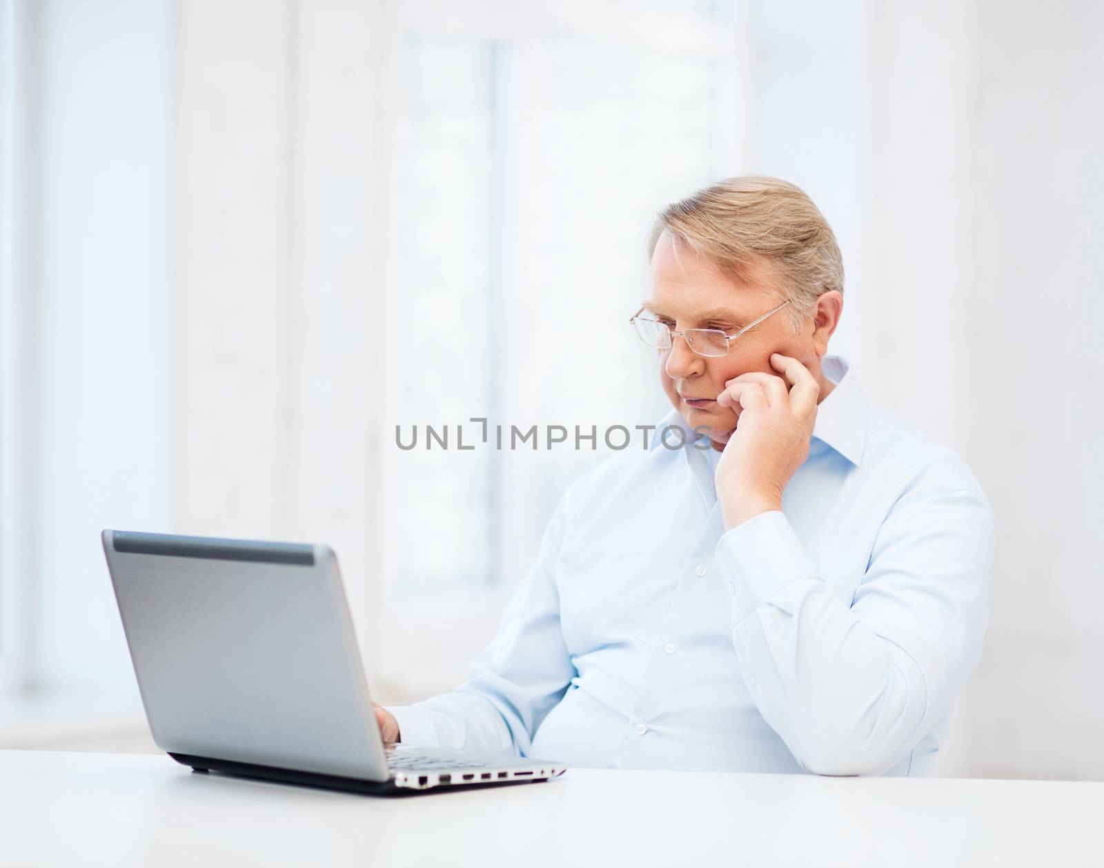 technology, oldness and lifestyle concept - old man in eyeglasses working with laptop computer at home
