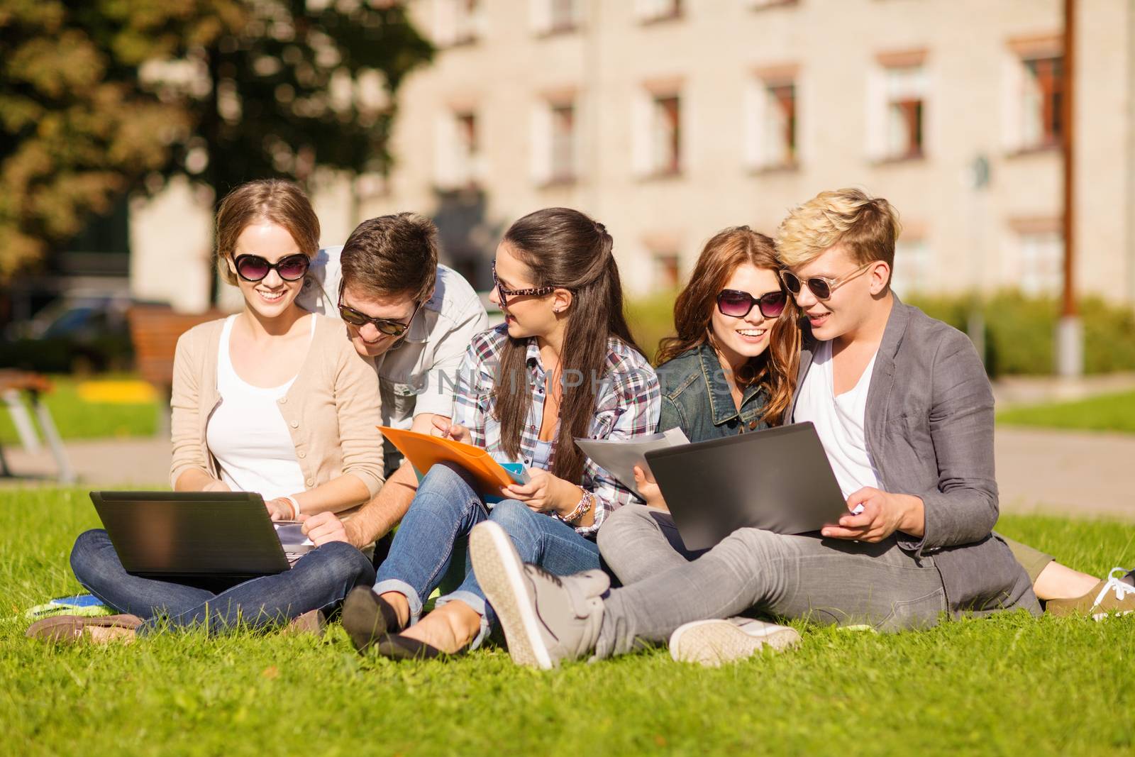 summer, internet, education, campus and teenage concept - group of students or teenagers with laptop, notebooks, files and folders