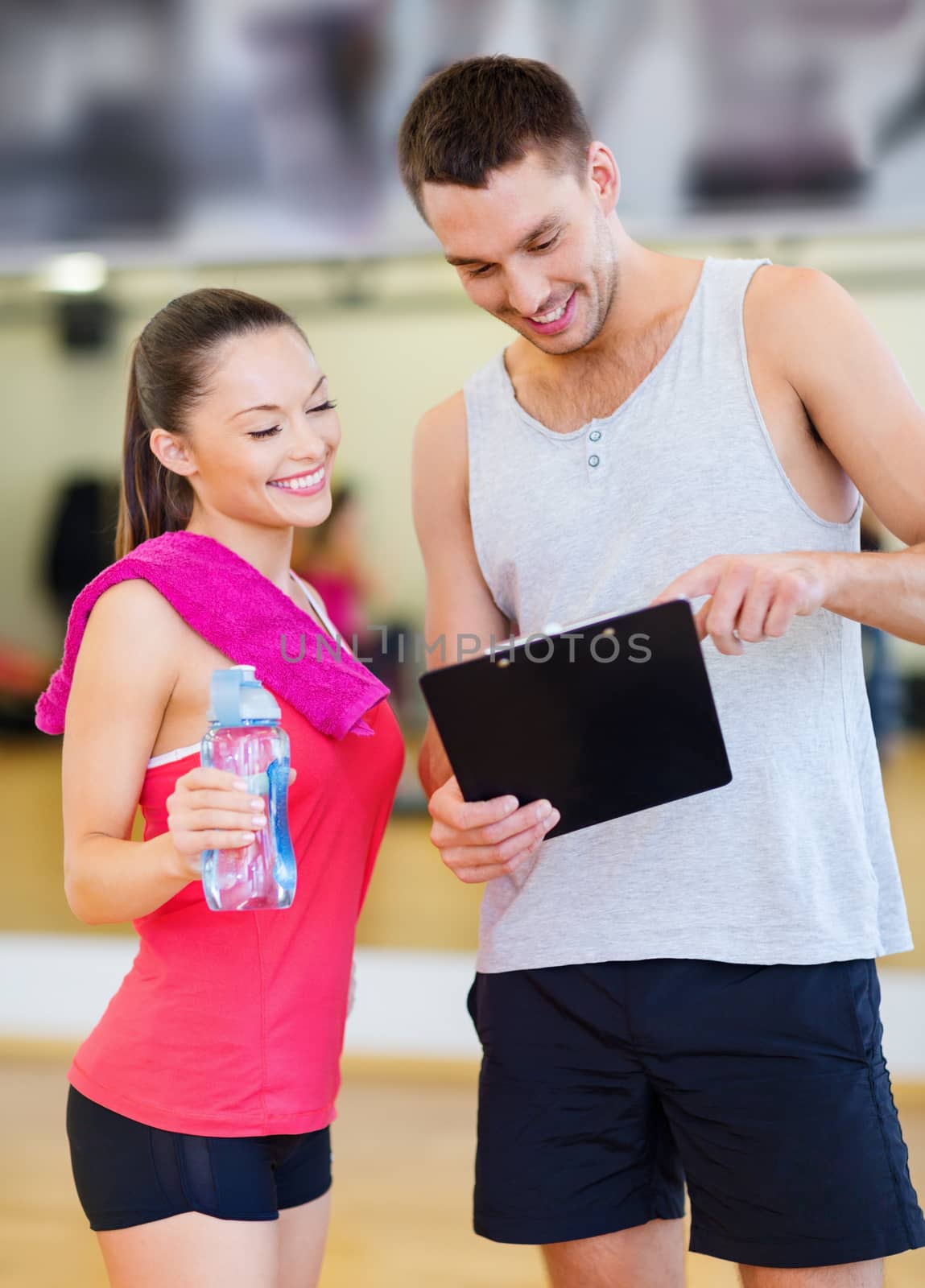 fitness, sport, training, gym and lifestyle concept - smiling male trainer with clipboard and woman with water bottle in the gym