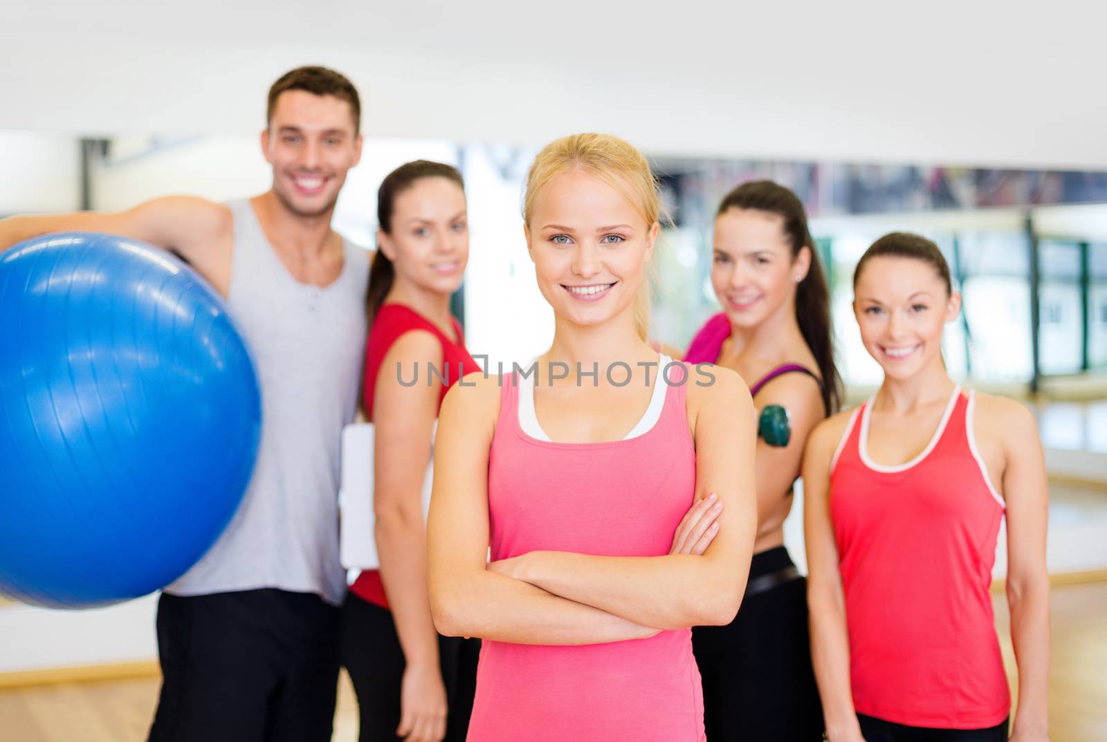 fitness, sport, training, gym and lifestyle concept - smiling woman standing in front of the group of people in gym