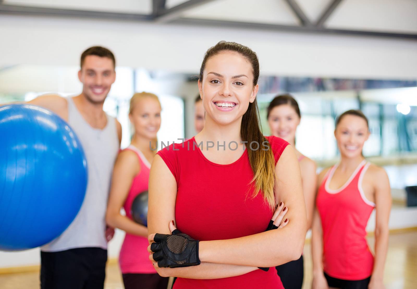 fitness, sport, training, gym and lifestyle concept - smiling woman standing in front of the group of people in gym