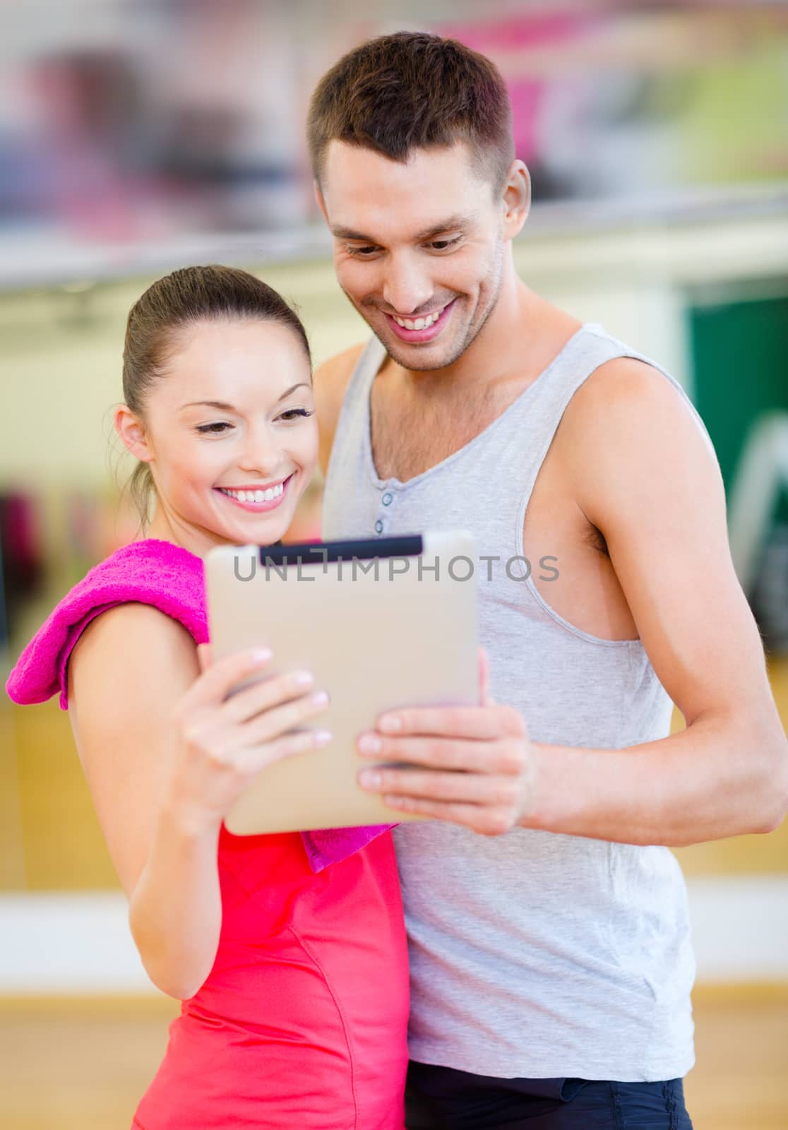 two smiling people with tablet pc in the gym by dolgachov