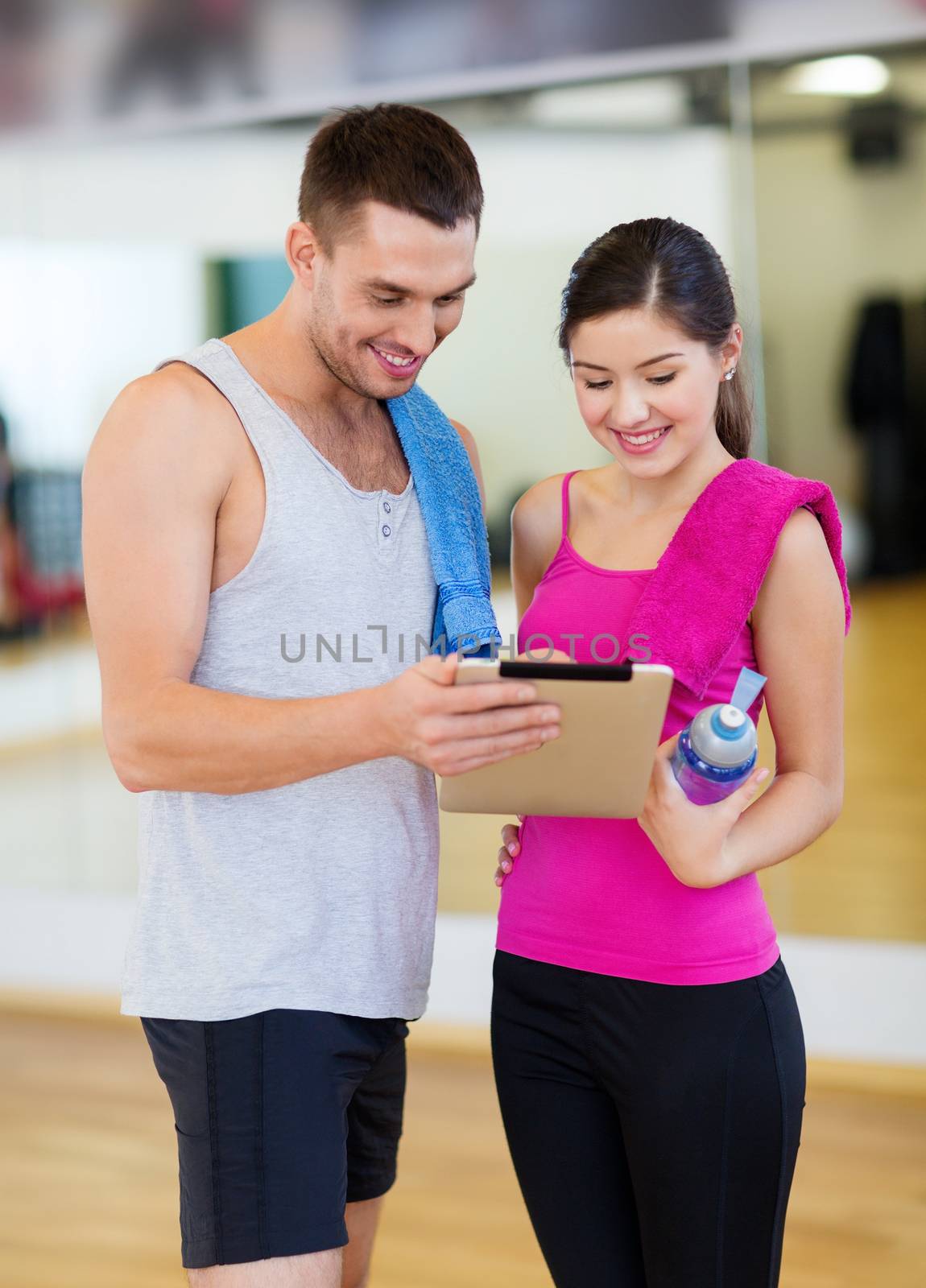 two smiling people with tablet pc in the gym by dolgachov