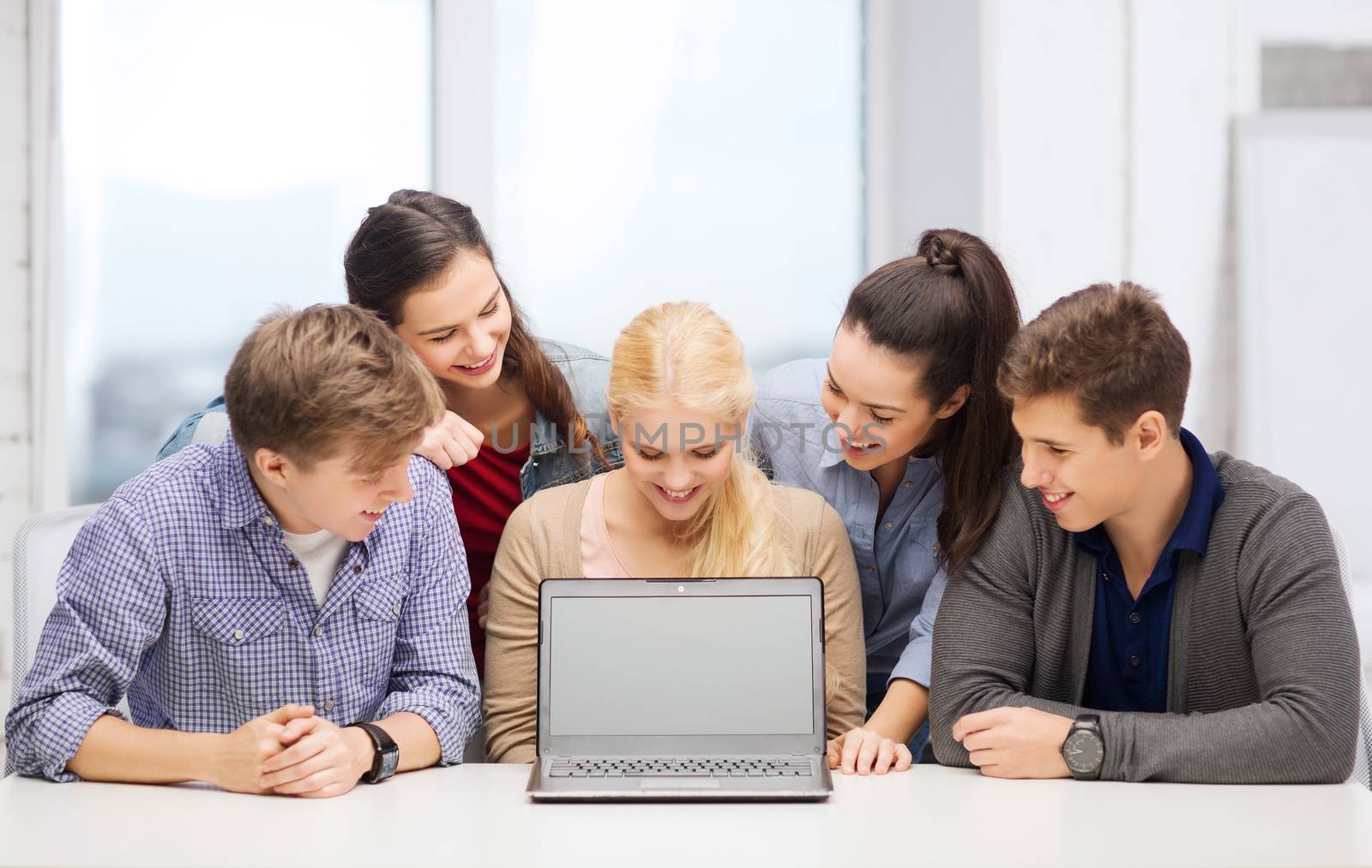 education, technology, advertisement and internet concept - group of smiling students looking at blank black laptop screen