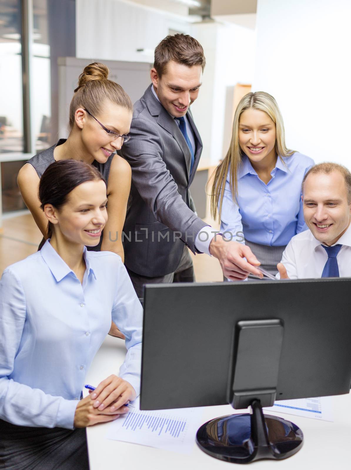 business, technology and office concept - smiling business team with computer monitor having discussion in office