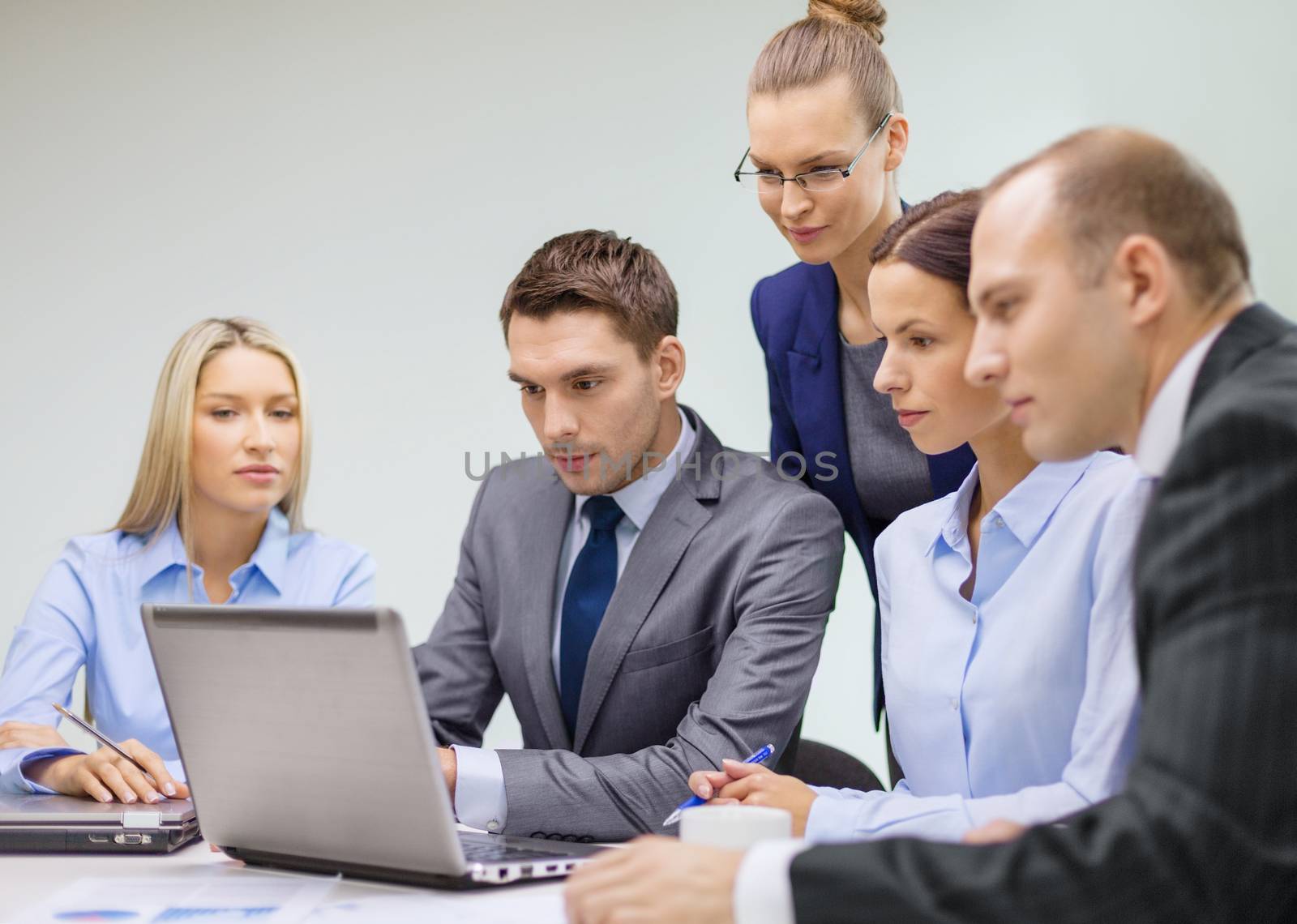 business, technology and office concept - serious business team with laptop computers, documents and coffee having discussion in office