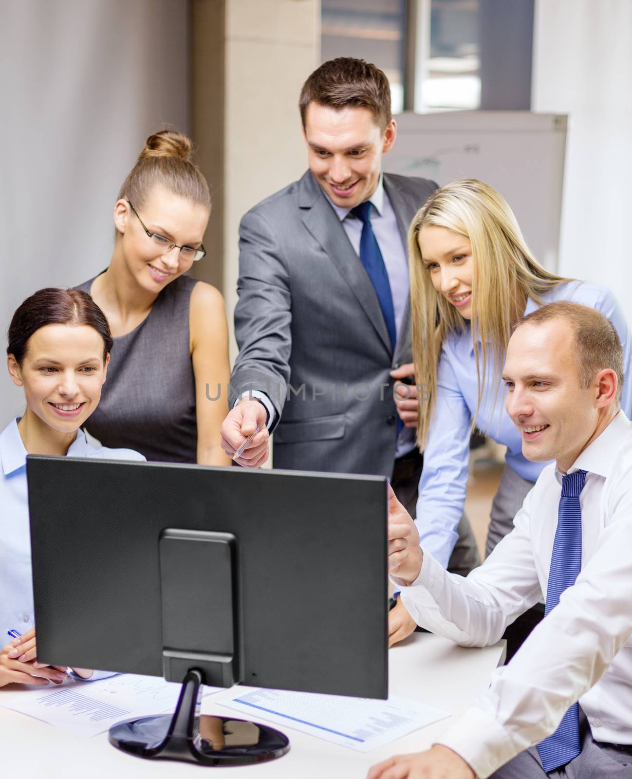 business, technology and office concept - smiling business team with computer monitor having discussion in office