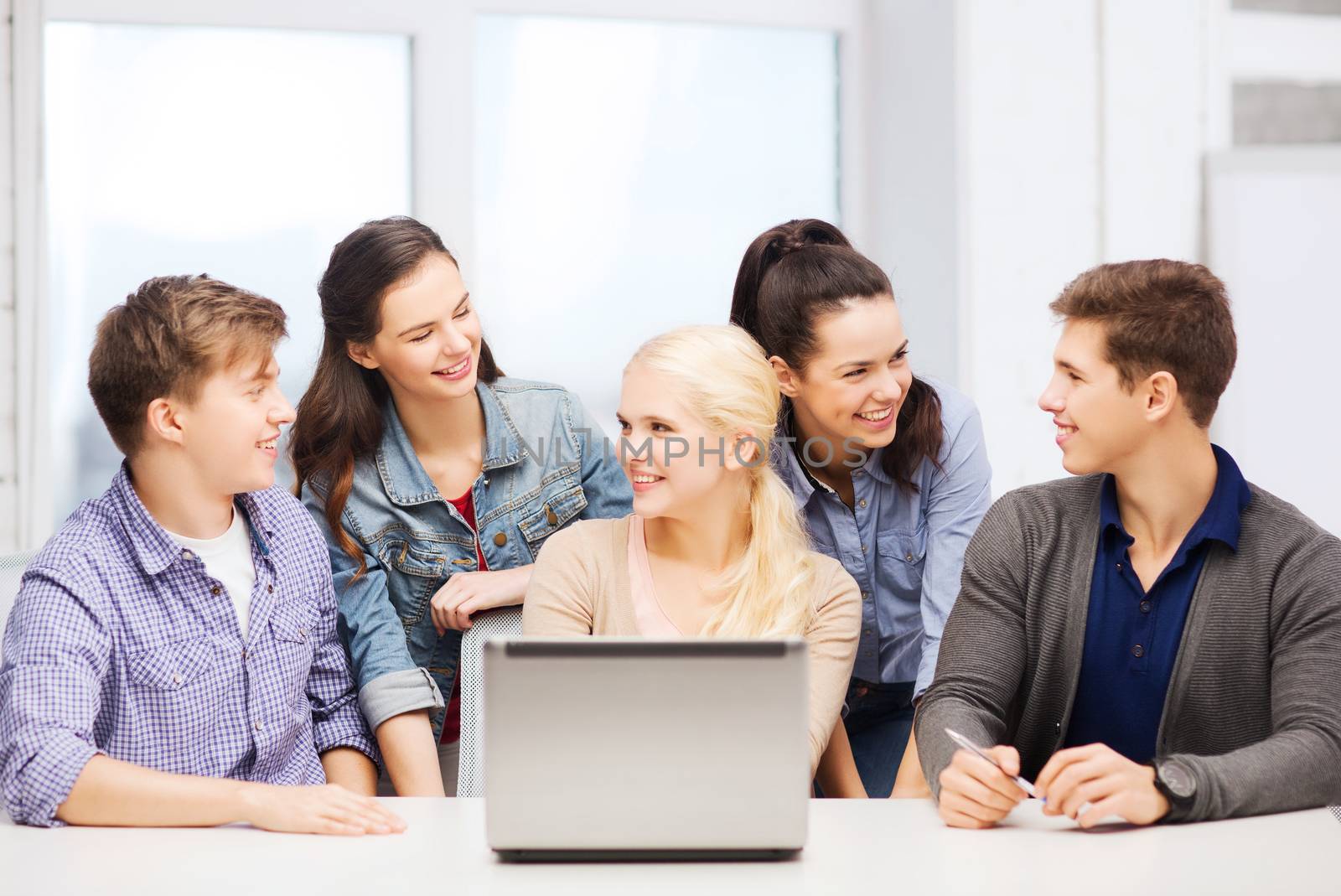 education, technology and internet concept - smiling students with laptop at school looking at each other