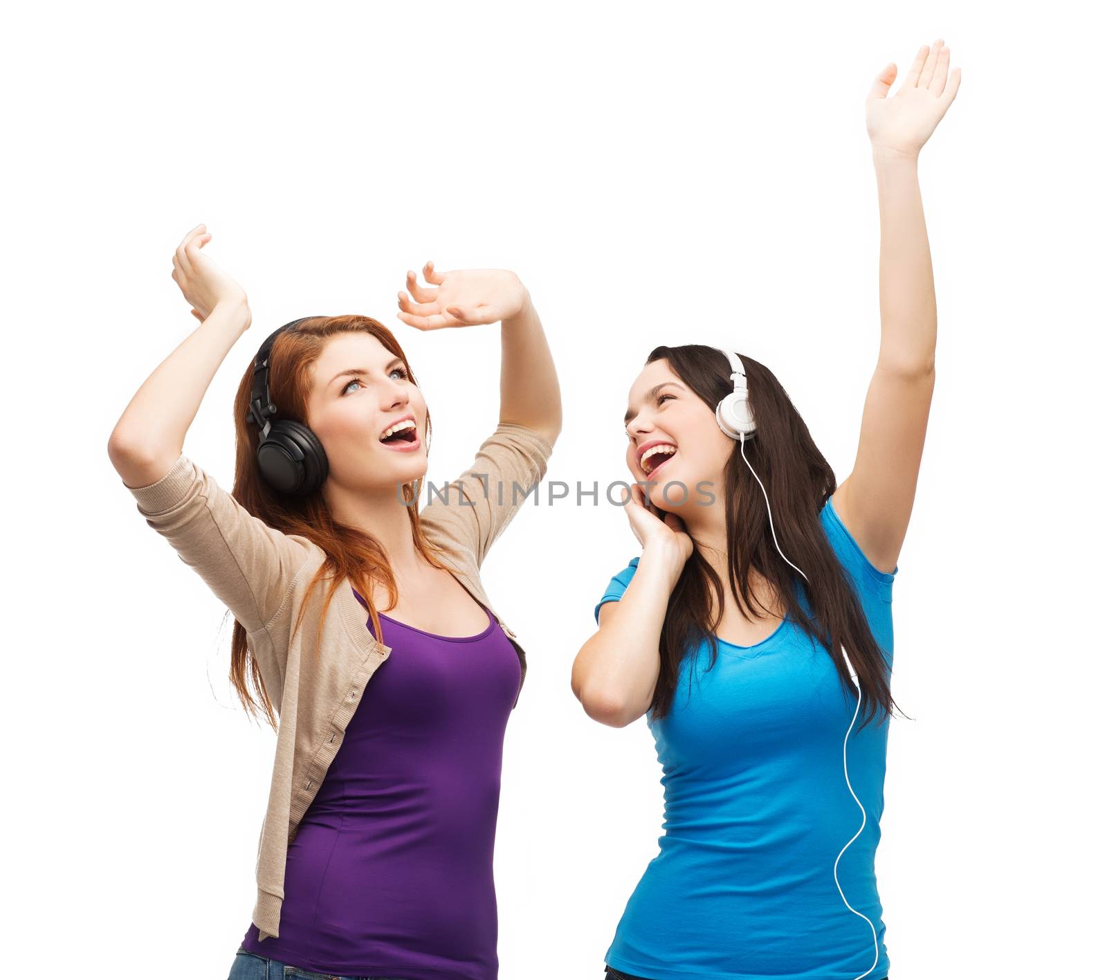 music and technology concept - two laughing teenagers with headphones dancing