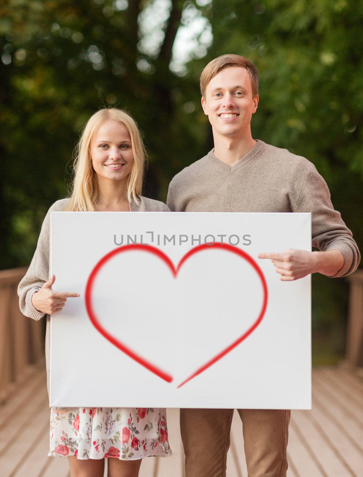 summer holidays, love, travel, relationship and advertisement concept - romantic couple on bridge pointing finger to white board with heart