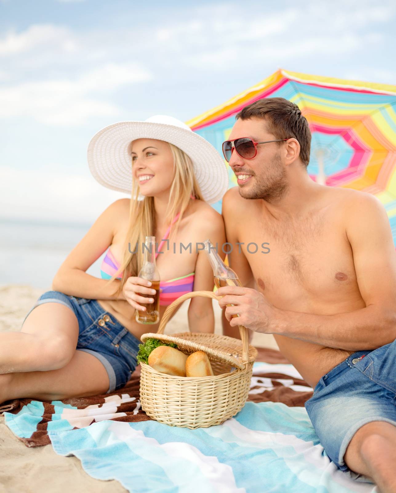 summer, holidays, vacation and happy people concept - smiling couple having picnic on the beach under colorful umbrella