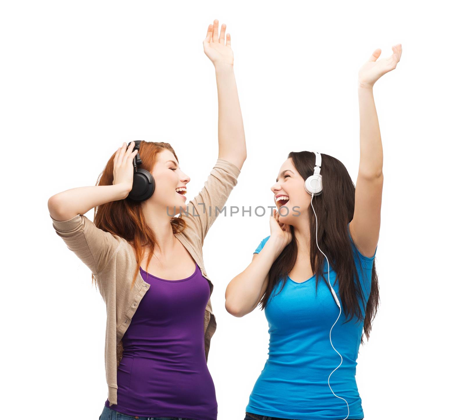 music and technology concept - two laughing teenagers with headphones dancing