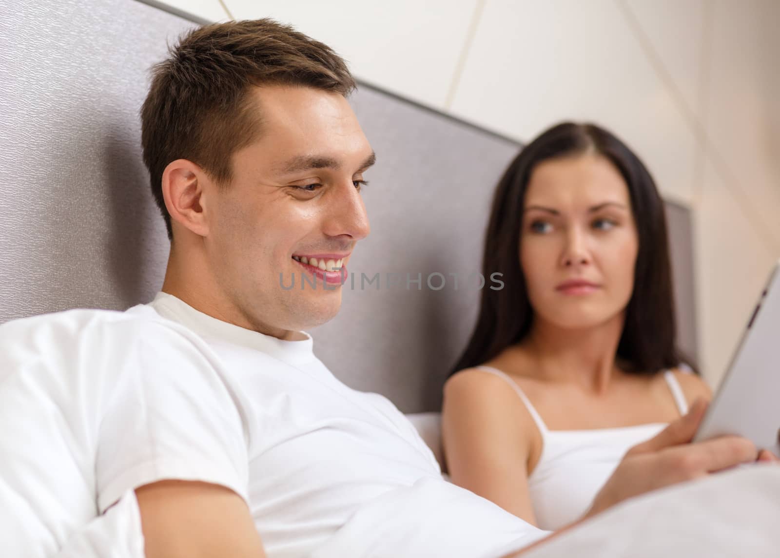 hotel, travel, relationships, technology, intermet and happiness concept - smiling couple in bed with tablet computer