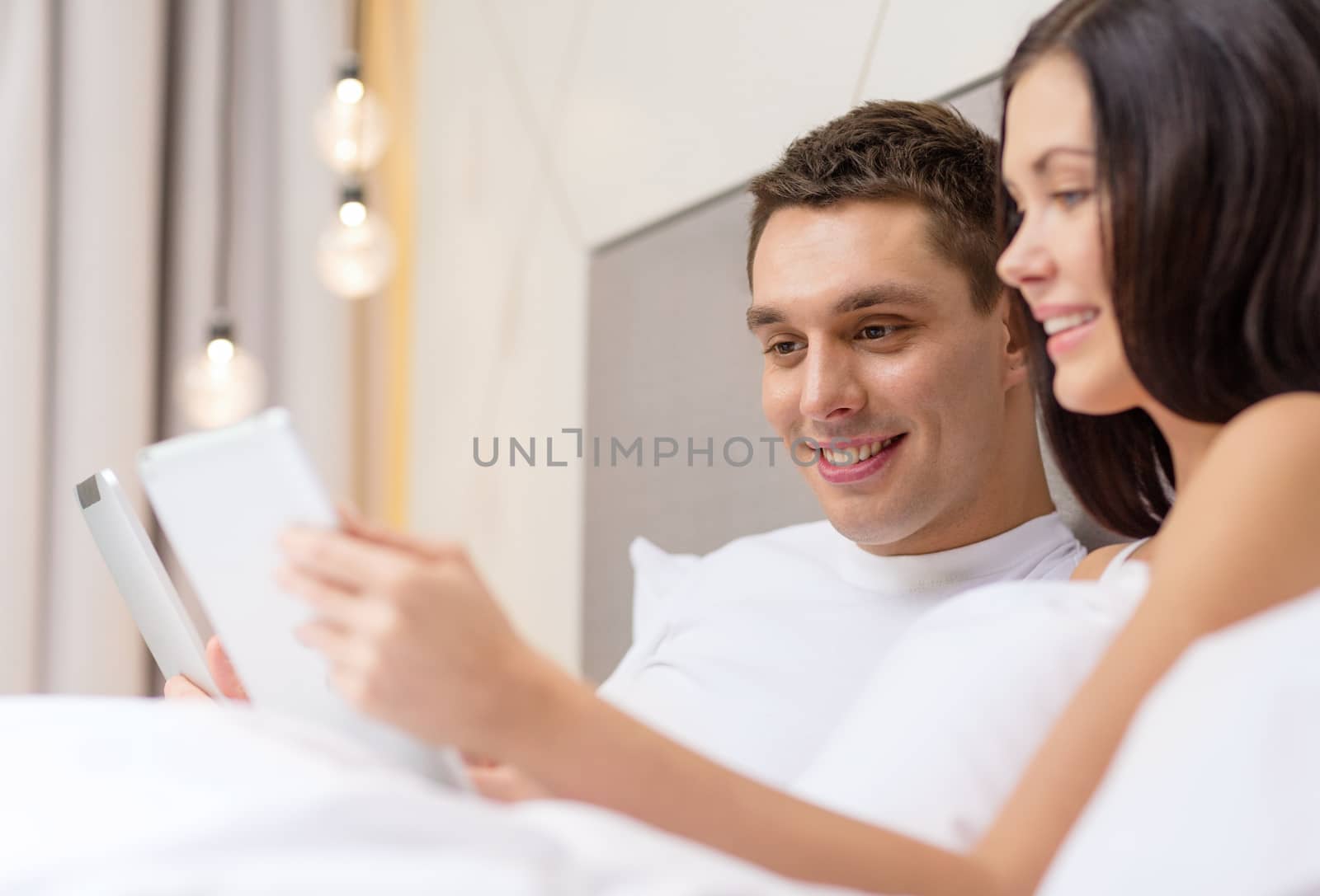 hotel, travel, relationships, technology, intermet and happiness concept - smiling couple in bed with tablet computers