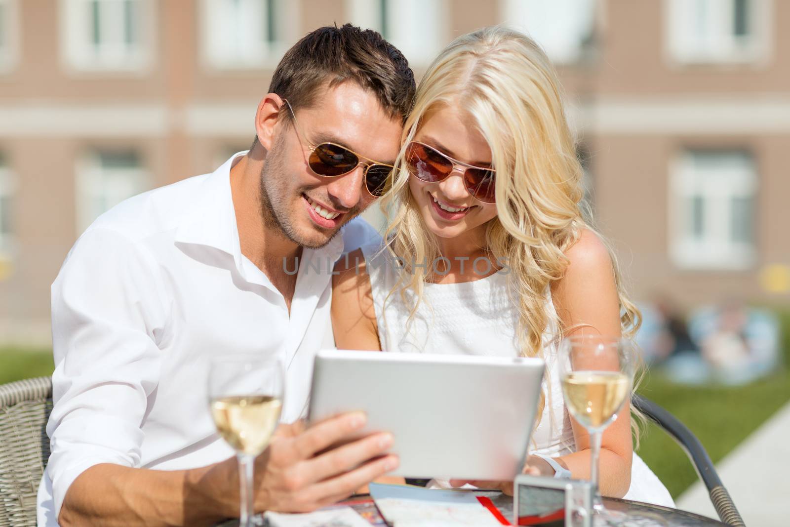 summer holidays, dating and technology concept - couple looking at tablet pc in cafe in the city