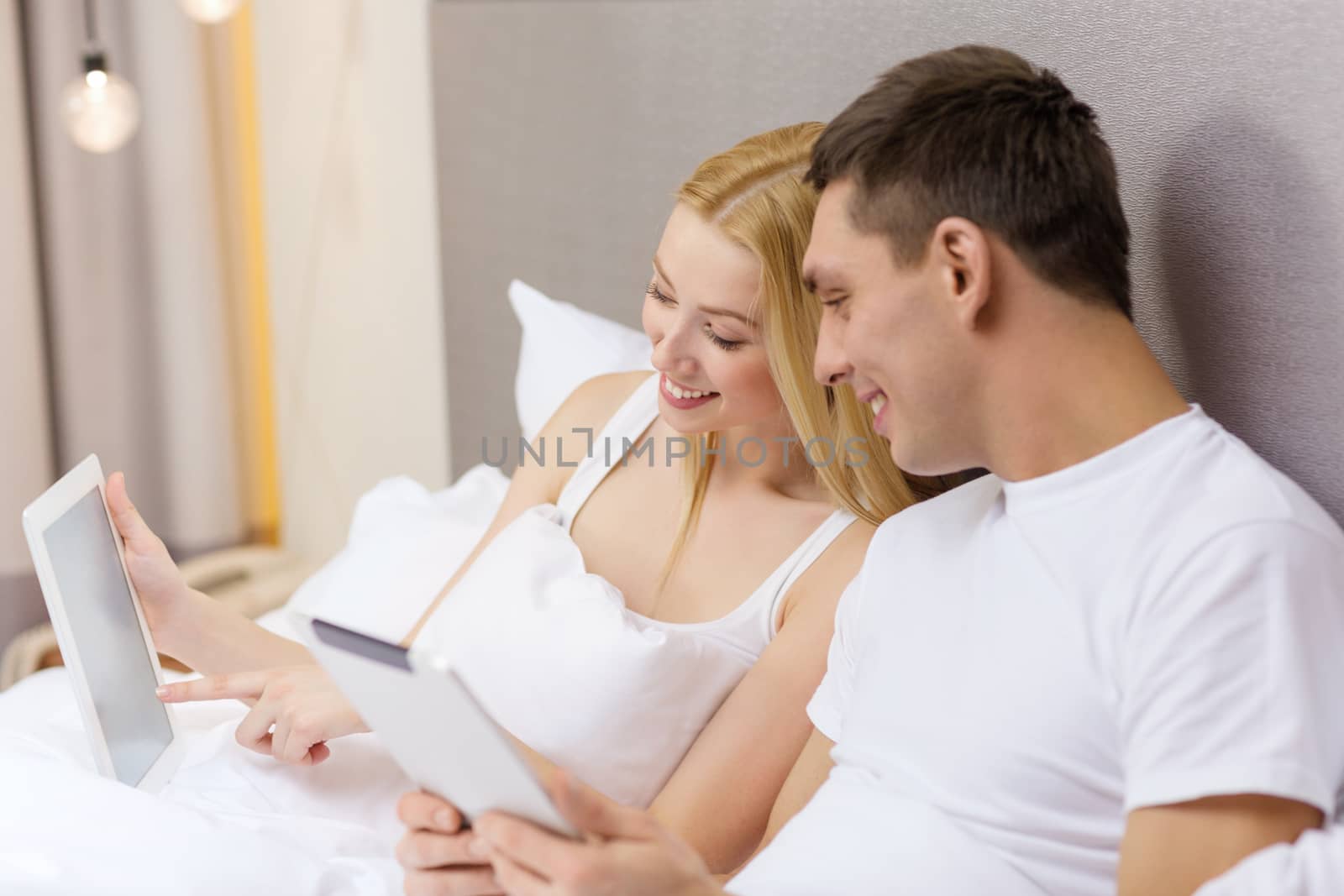 hotel, travel, relationships, technology, intermet and happiness concept - smiling couple in bed with tablet computers