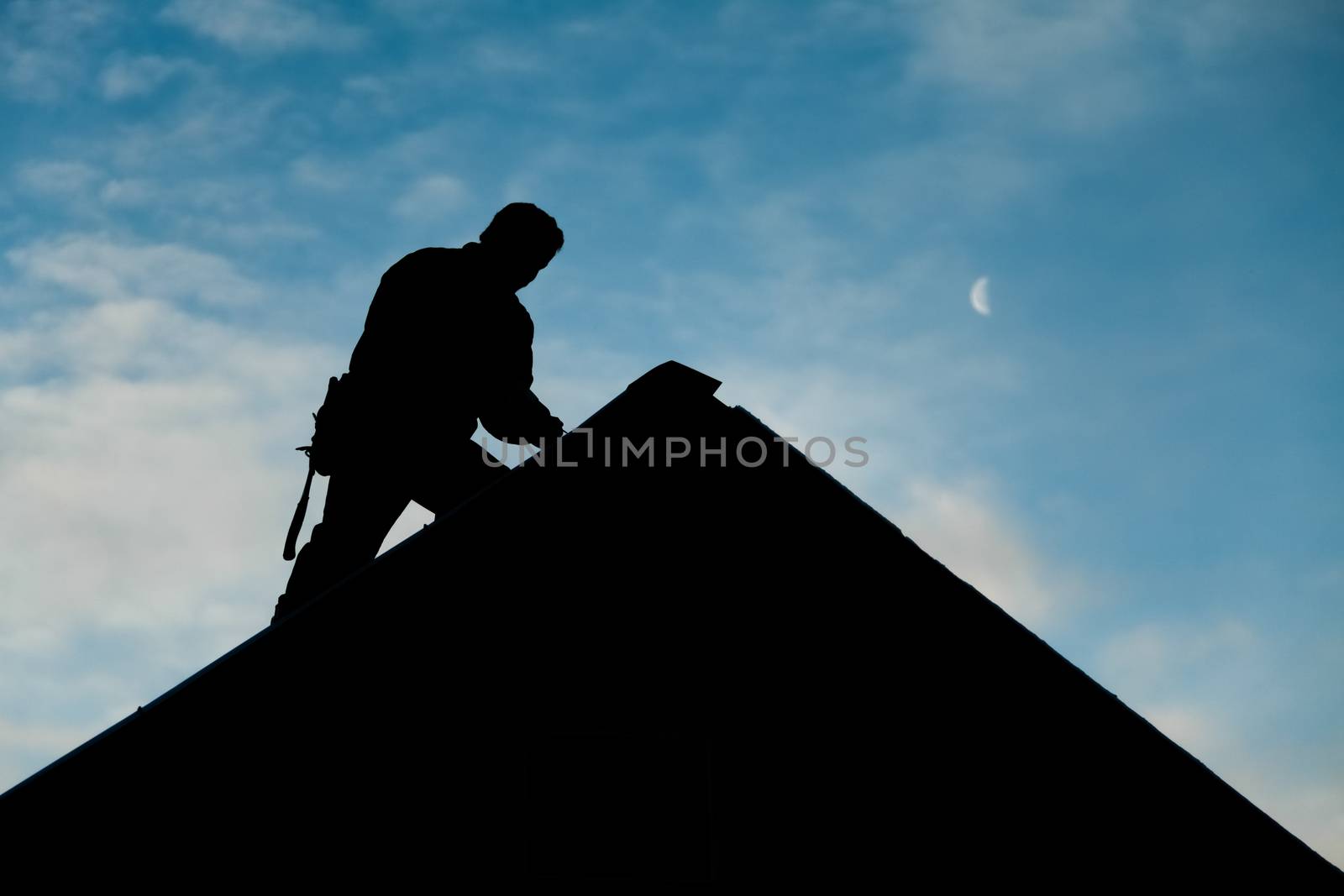 Contractor in Silhouette working on a Roof Top with blue Sky in Background