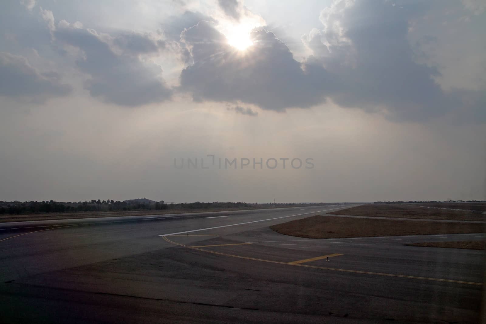 the sun shining through a layer of rain cluds as a  burst of white  light over an airport runway 