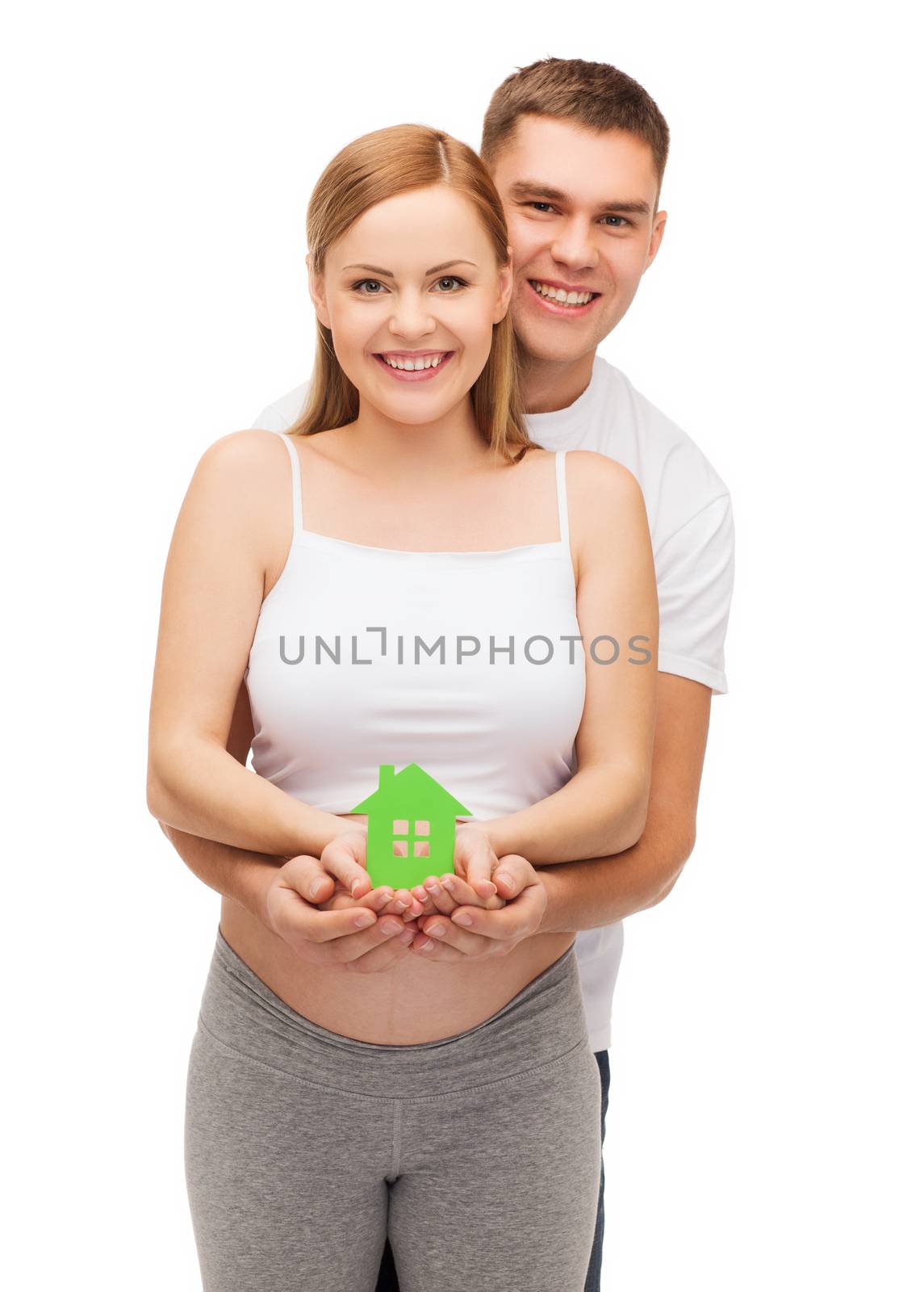 pregnancy, parenthood, real estate and happiness concept - happy young family expecting child showing green paper house