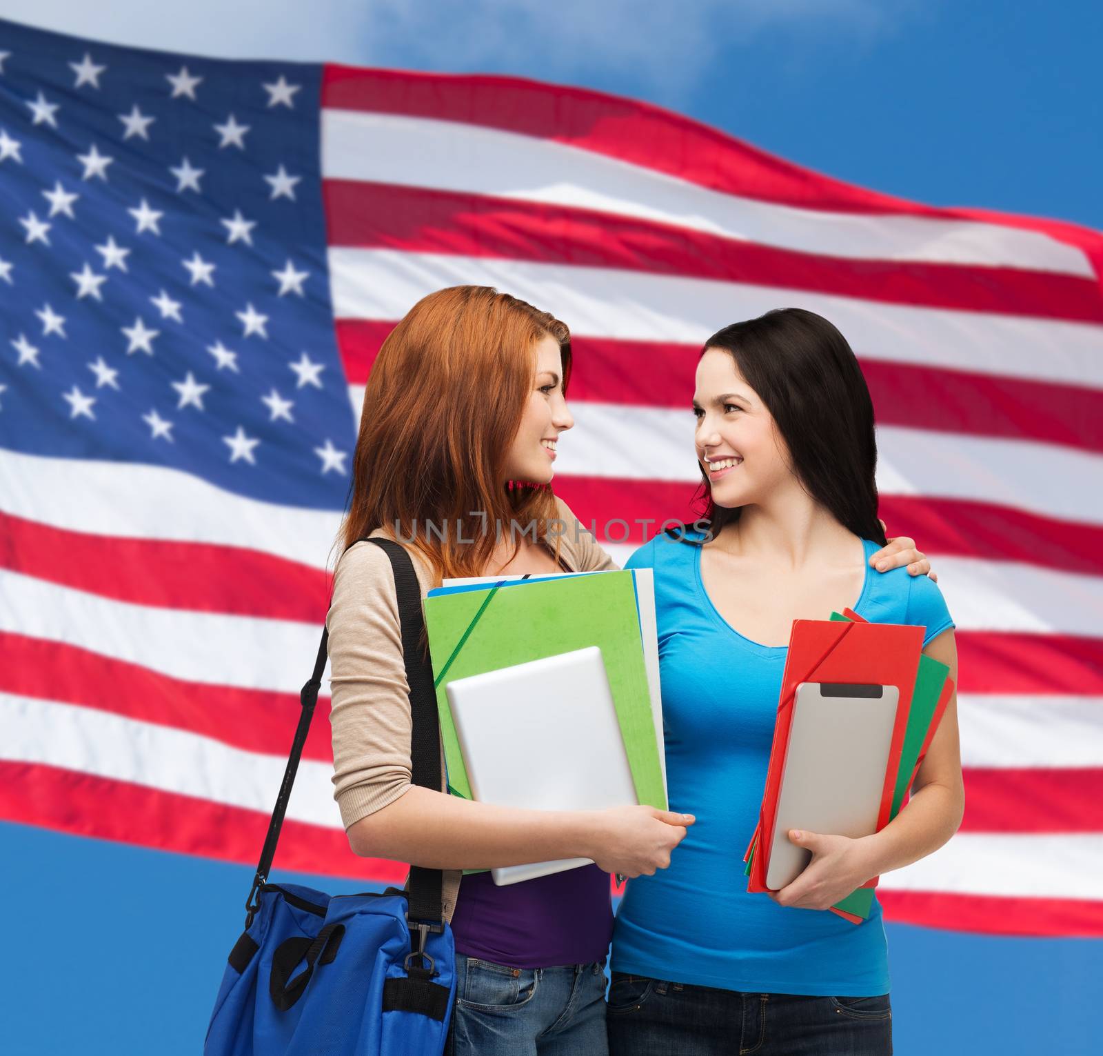 education and people concept - two smiling students with bag and folders looking at each other over american flag background