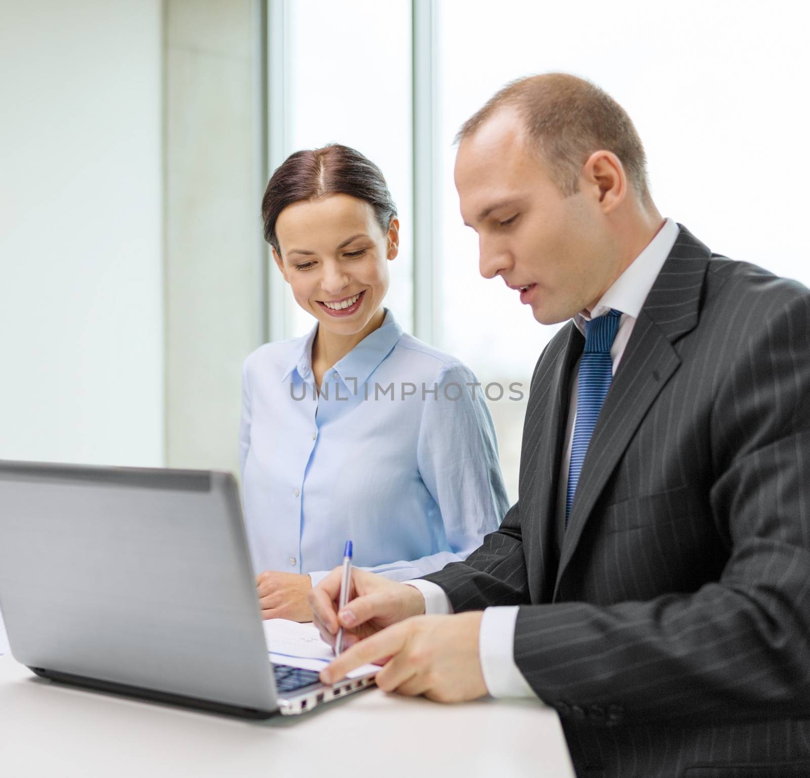 business, technology and office concept - smiling business team with laptop computer and documents having discussion in office