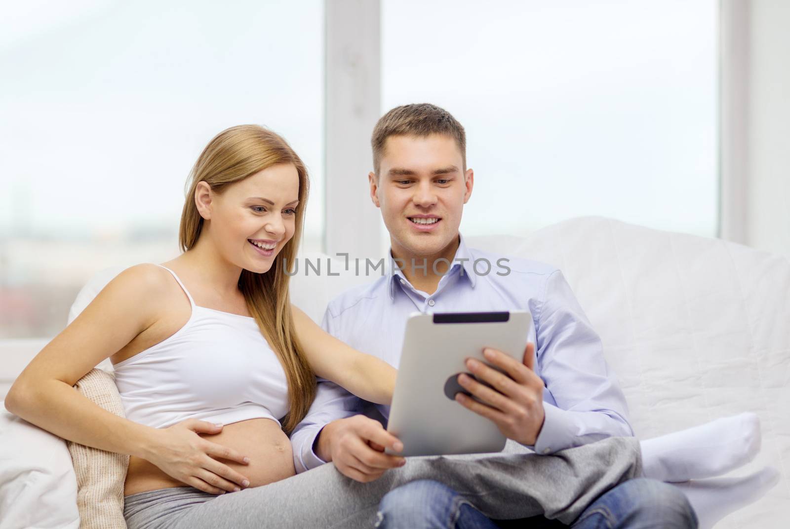 pregnancy, parenthood, internet and technology concept - expecting family with tablet pc computer