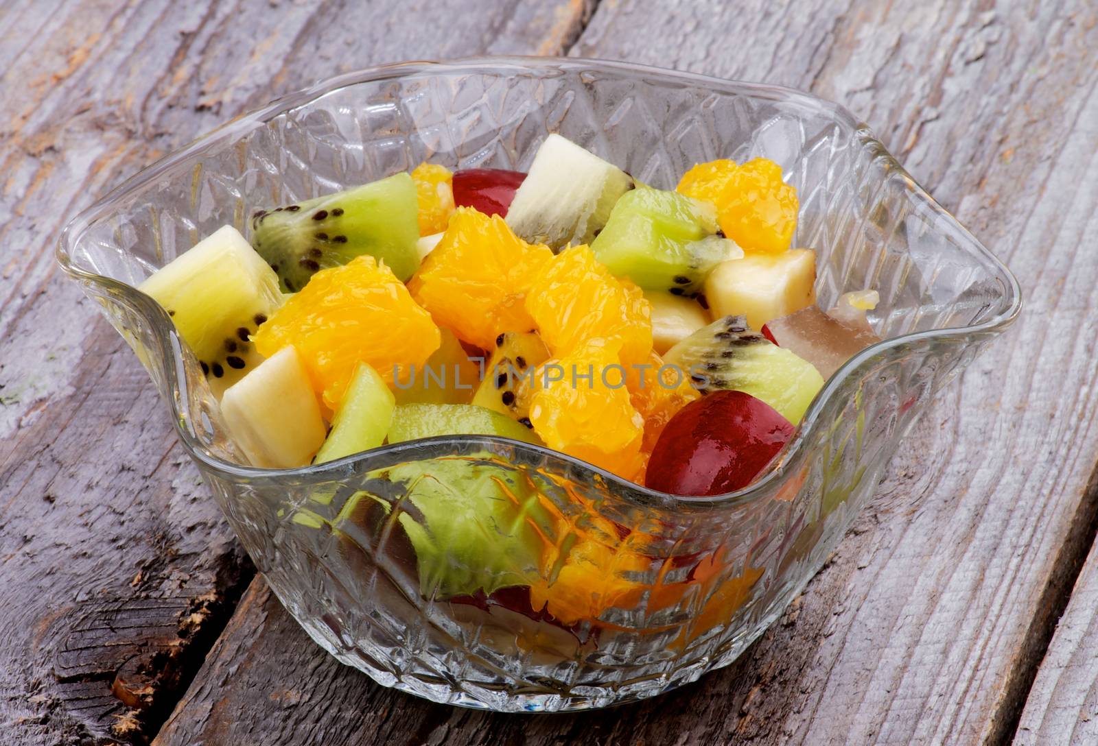 Fruit Salad with Red Grape, Green and Golden Kiwi, Bananas and Oranges in Glass Bowl isolated on Wooden background