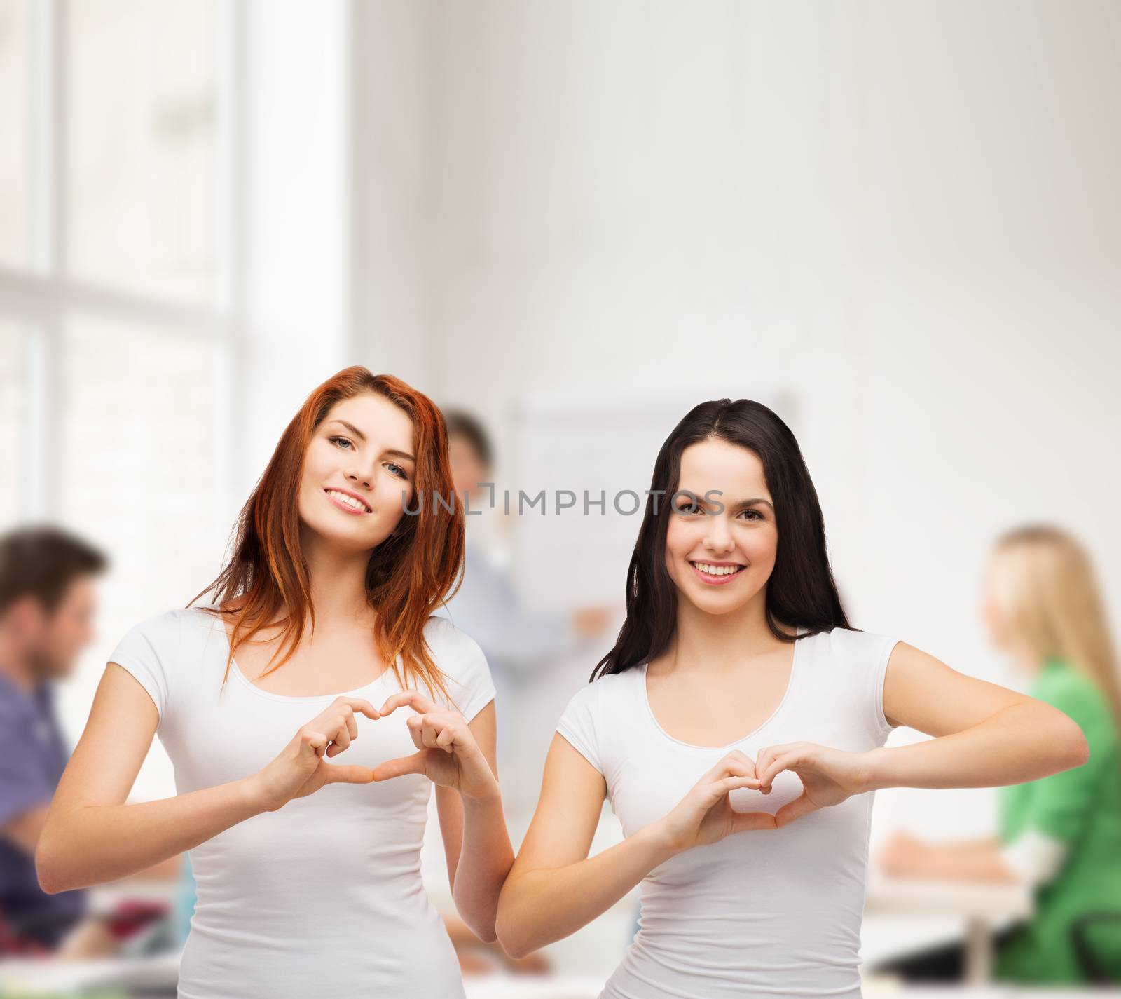 friendship, education and happy people concept - two smiling girls in white t-shirts showing heart with hands
