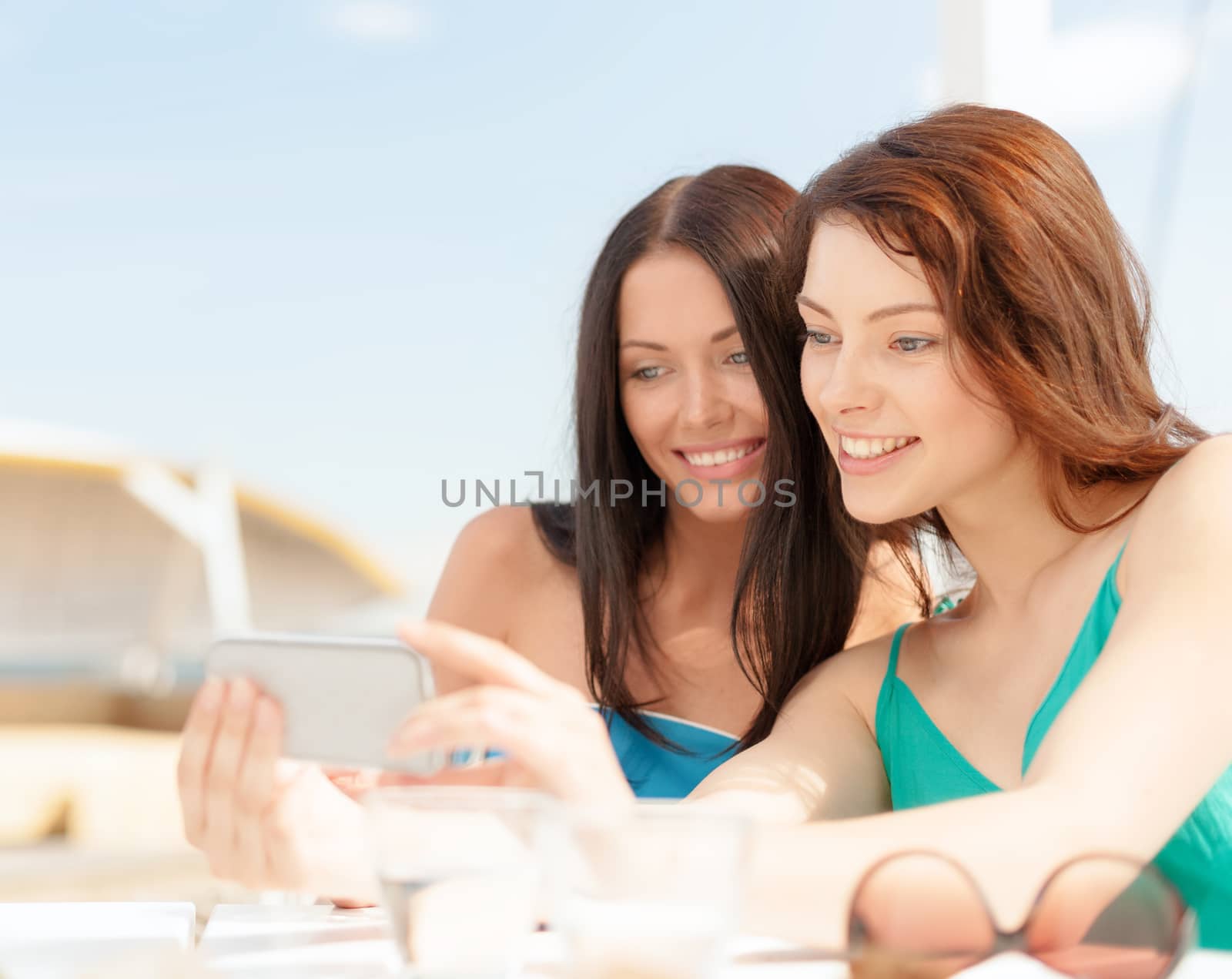 summer holidays, vacation and technology concept - girls looking at smartphone in cafe on the beach