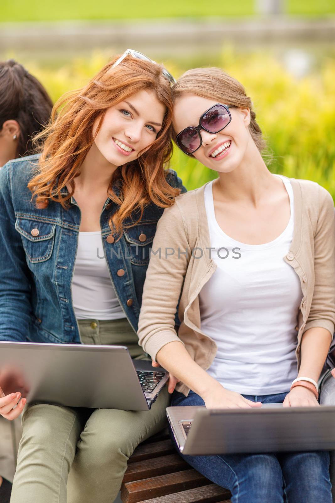 summer holidays, education, campus, technology and teenage concept - two female students with laptop computers