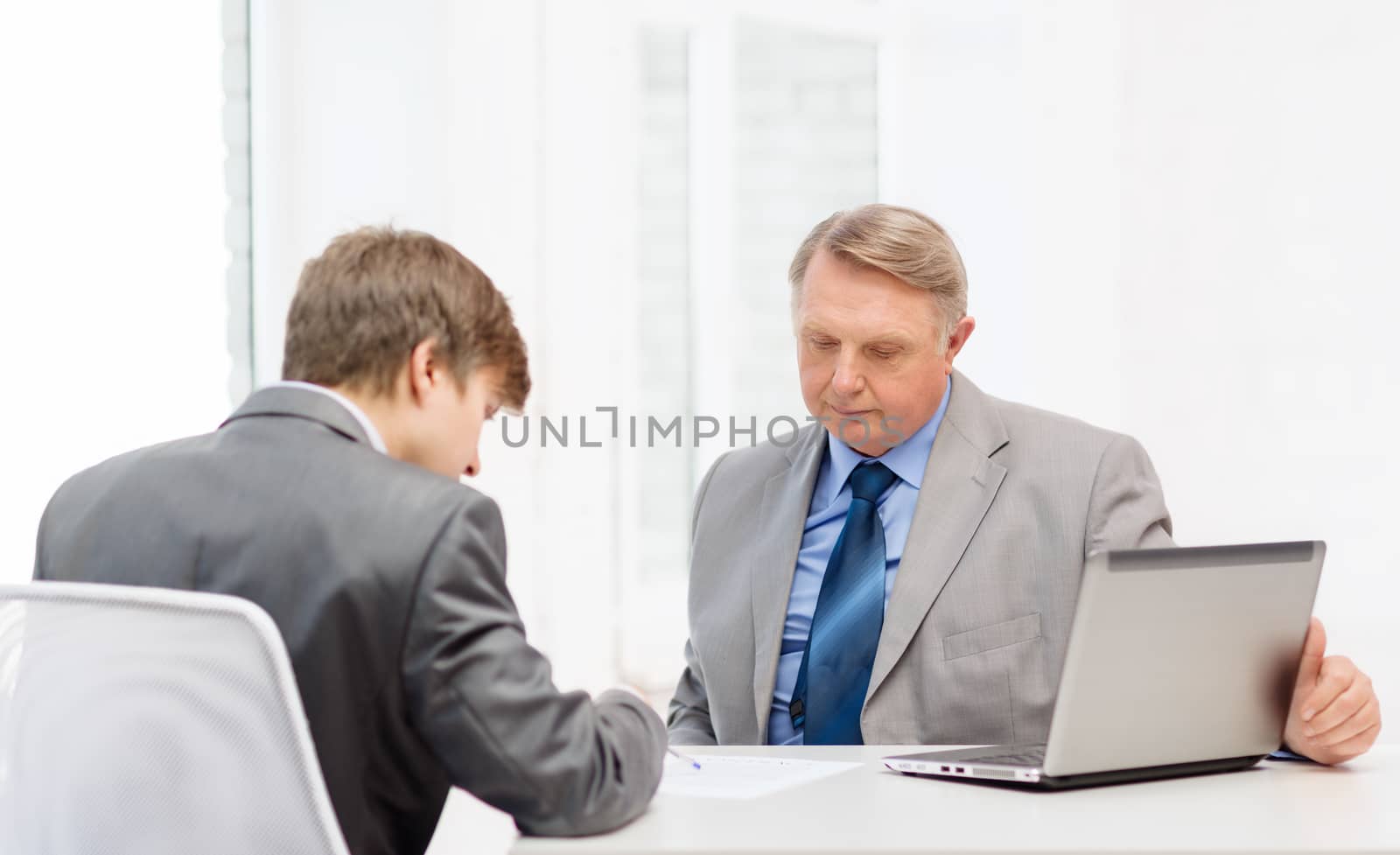 business, technology and office concept - older man and young man signing papers in office